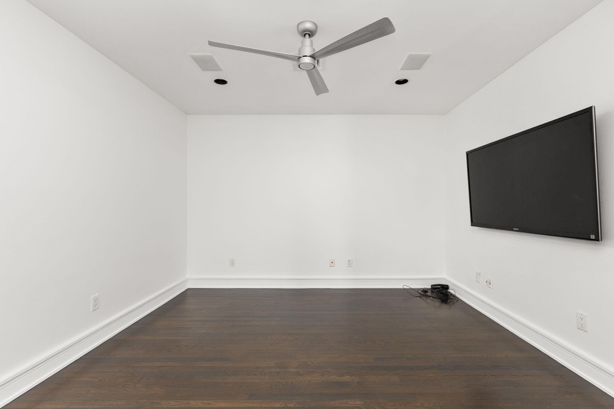 Empty room with dark wood floors, a ceiling fan, and a wall-mounted television.