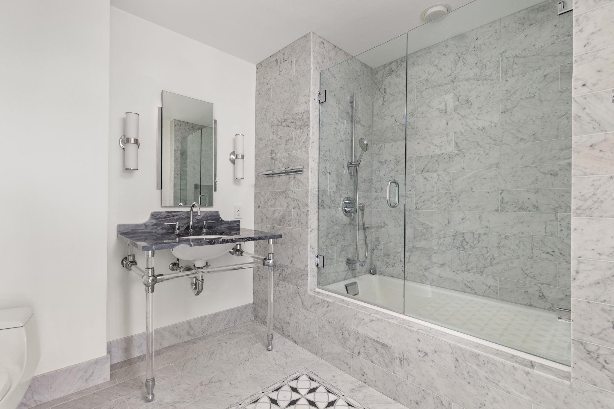 Bathroom with marble tile, glass shower enclosure, and dark stone vanity with exposed metal legs.