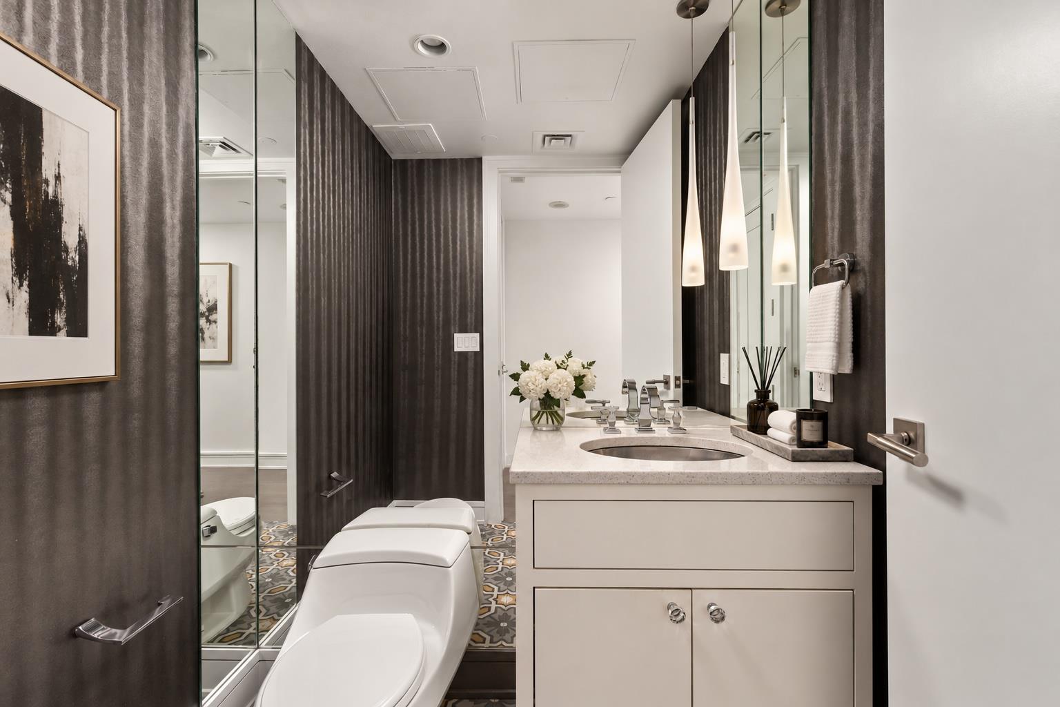 Bathroom with a white vanity, mirrored walls, patterned tile floor, and modern toilet.
