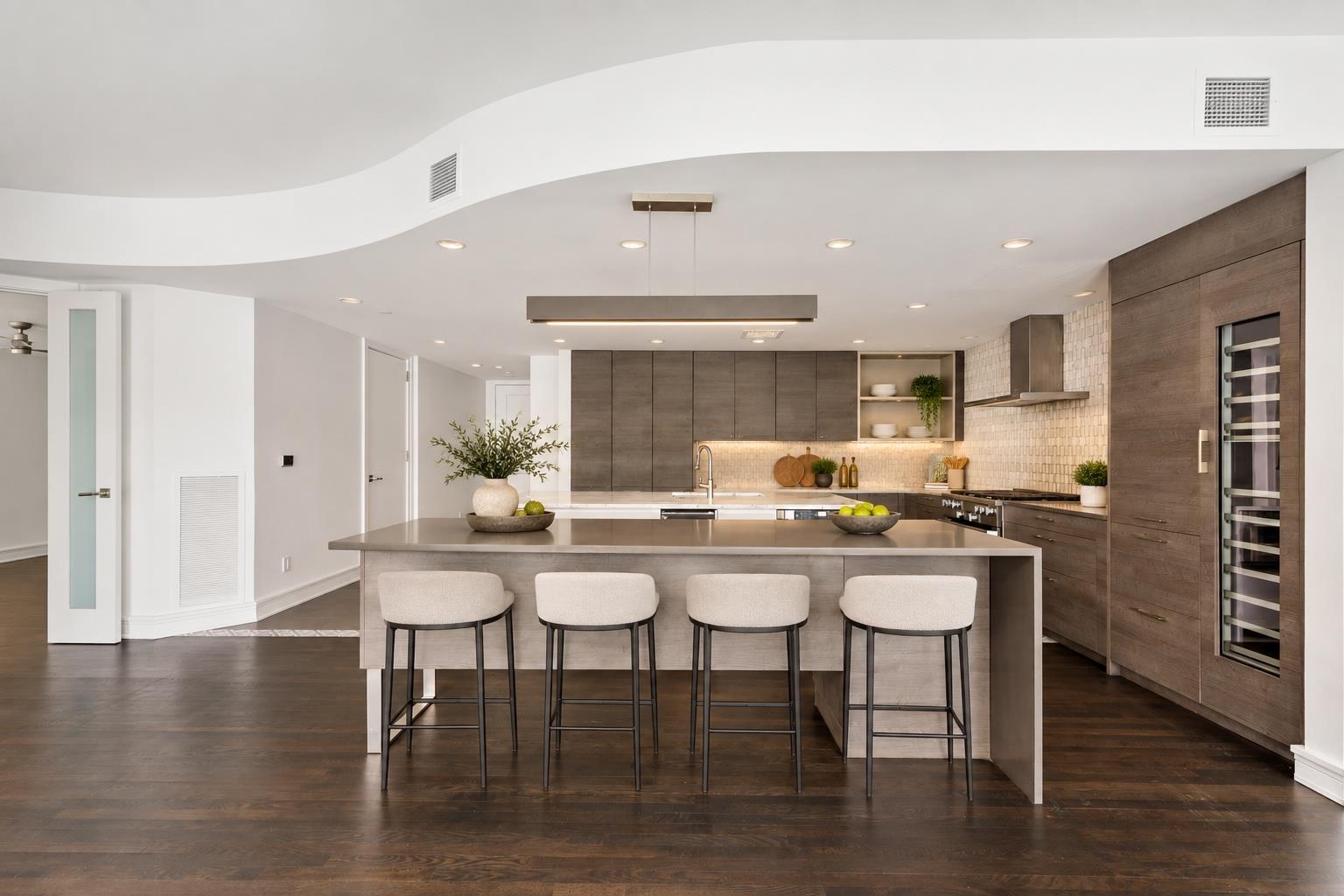 Modern kitchen with a large island, four stools, dark wood cabinetry, and a built-in wine refrigerator.