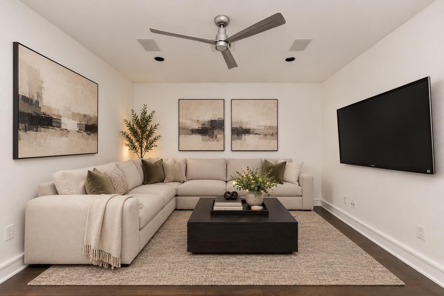 Staged living room with a cream sectional, abstract wall art, dark coffee table, and wall-mounted television.