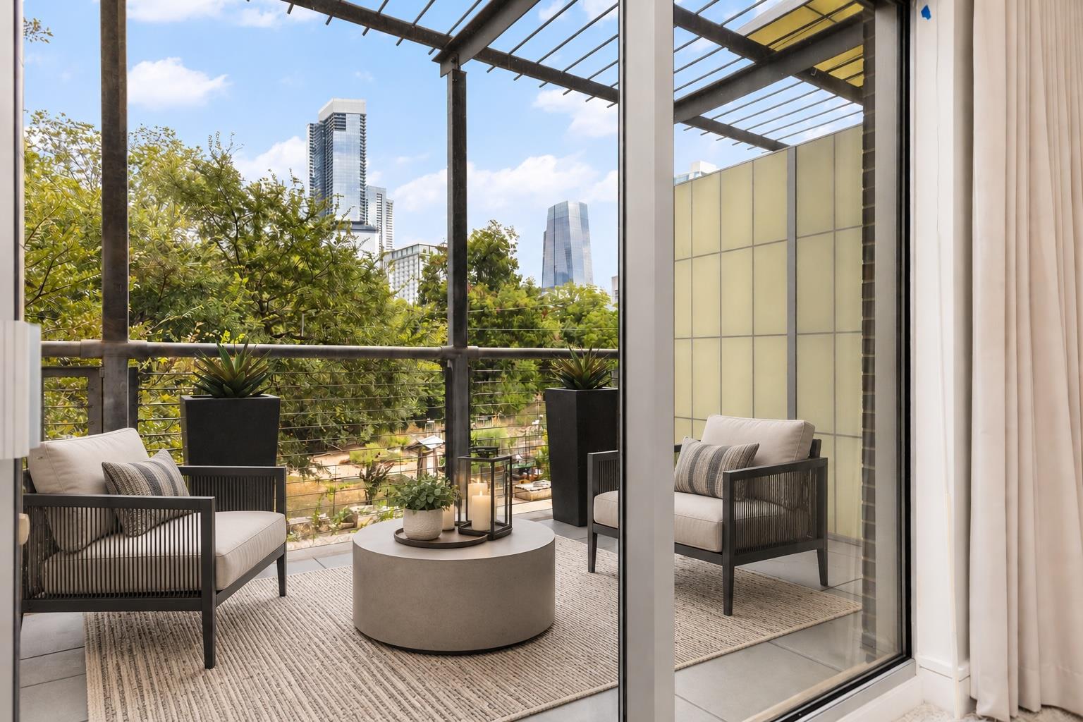 Condo balcony with cushioned seating, potted plants, and a view of downtown high-rises.