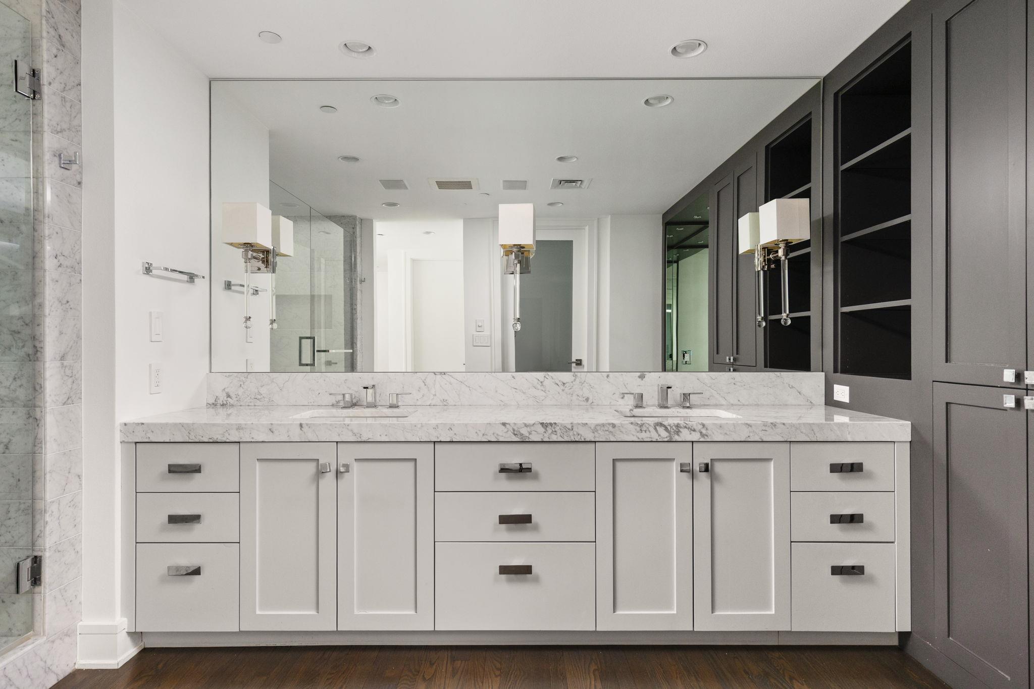 Bathroom with a double-sink marble vanity, large mirror, and dark built-in cabinetry.
