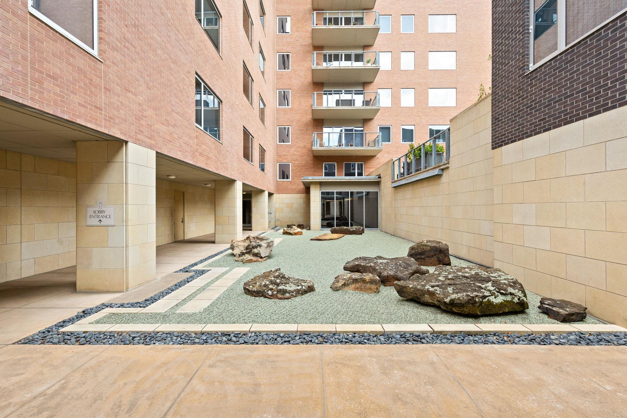 Condominium courtyard with gravel landscaping, decorative rocks, and a sign pointing to the lobby entrance.