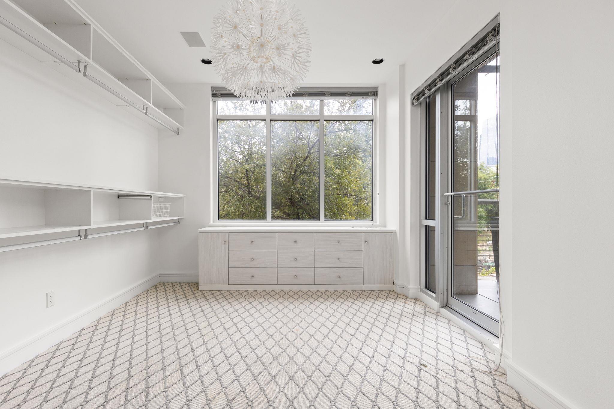 Bright dressing room with built-in white shelving, patterned carpet, and a glass door to the balcony.