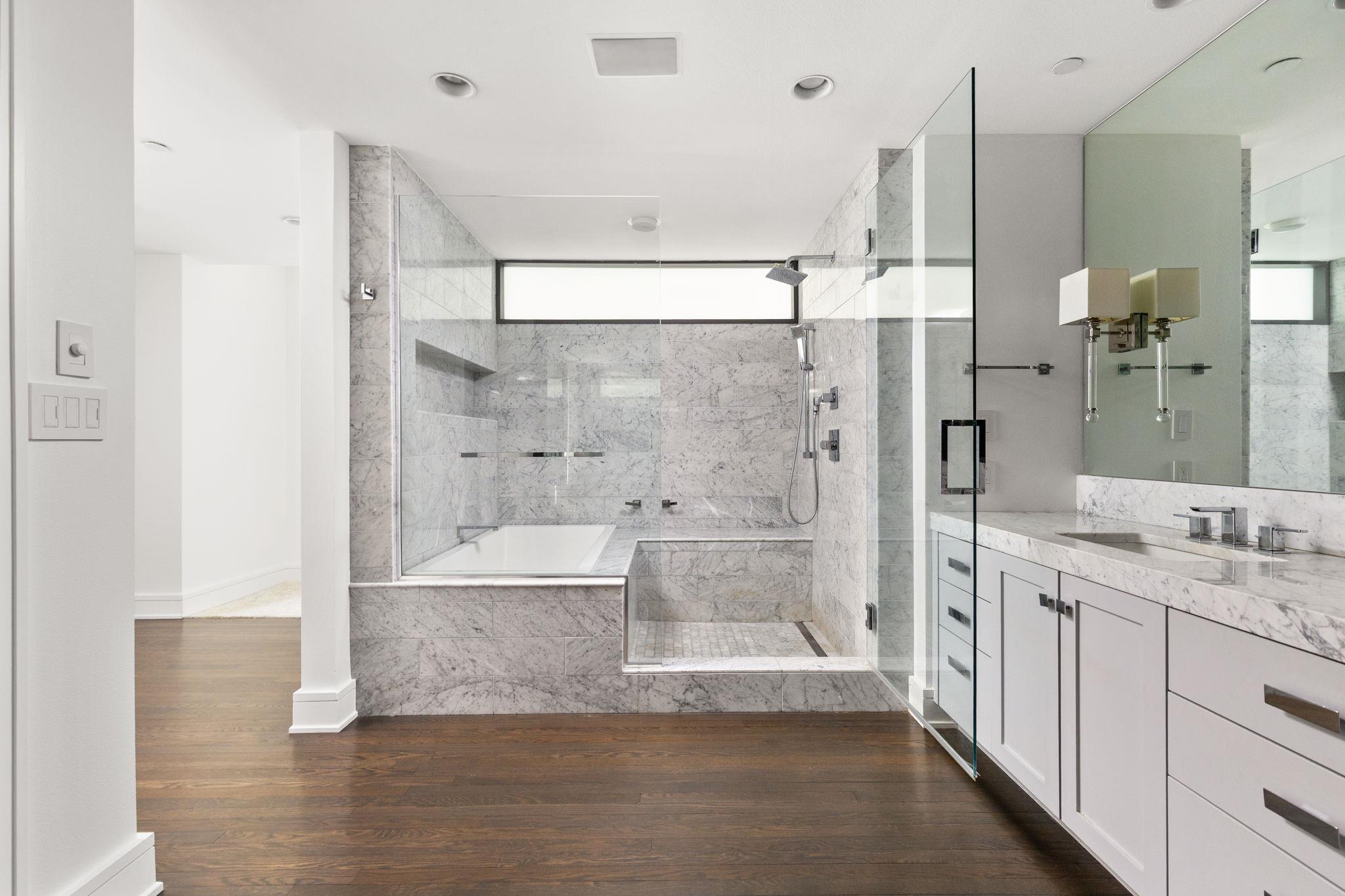 Marble bathroom with glass shower, built-in soaking tub, and long double vanity.