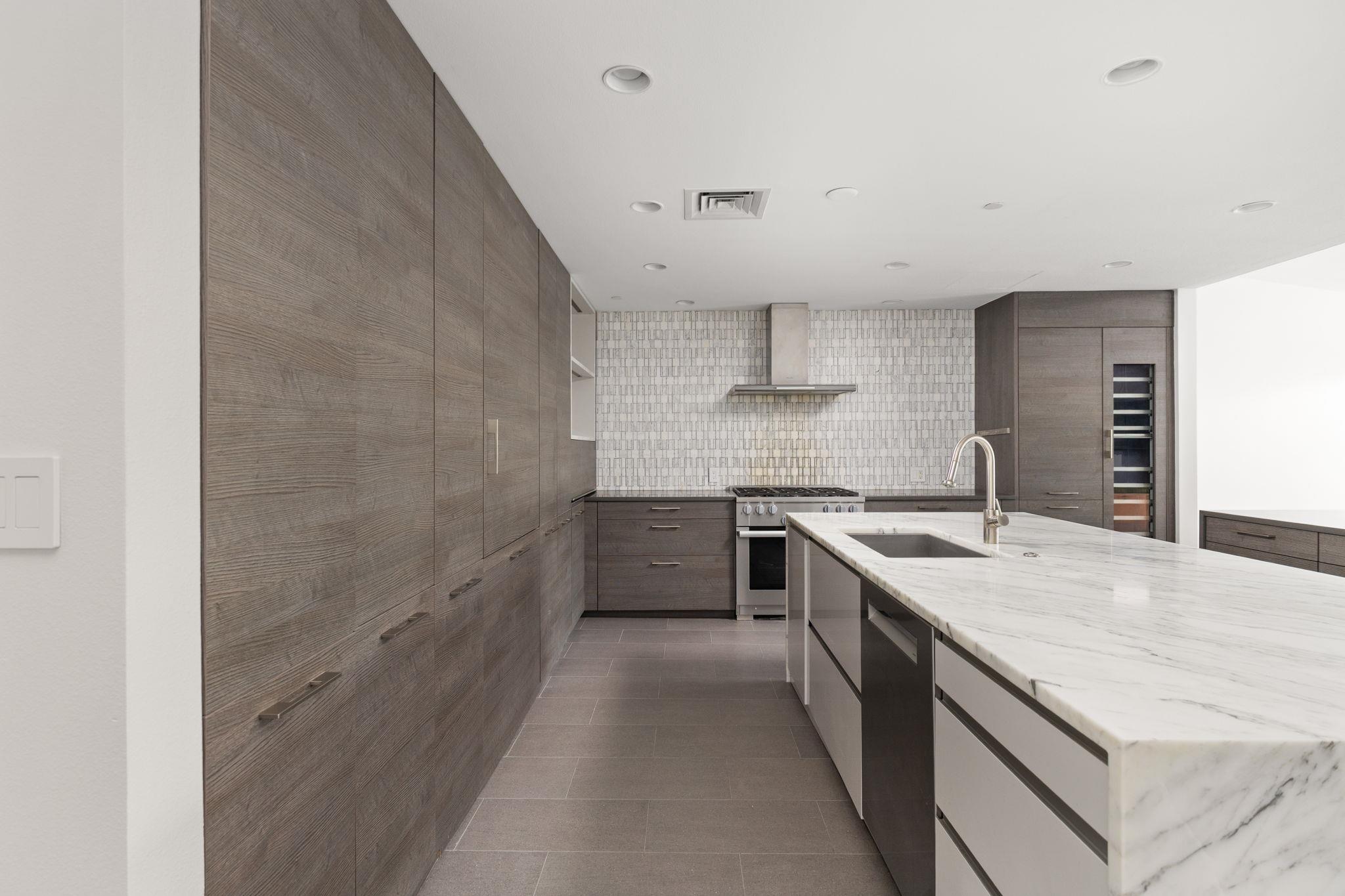Modern kitchen with a marble island, dark wood cabinets, patterned tile backsplash, and built-in wine refrigerator.