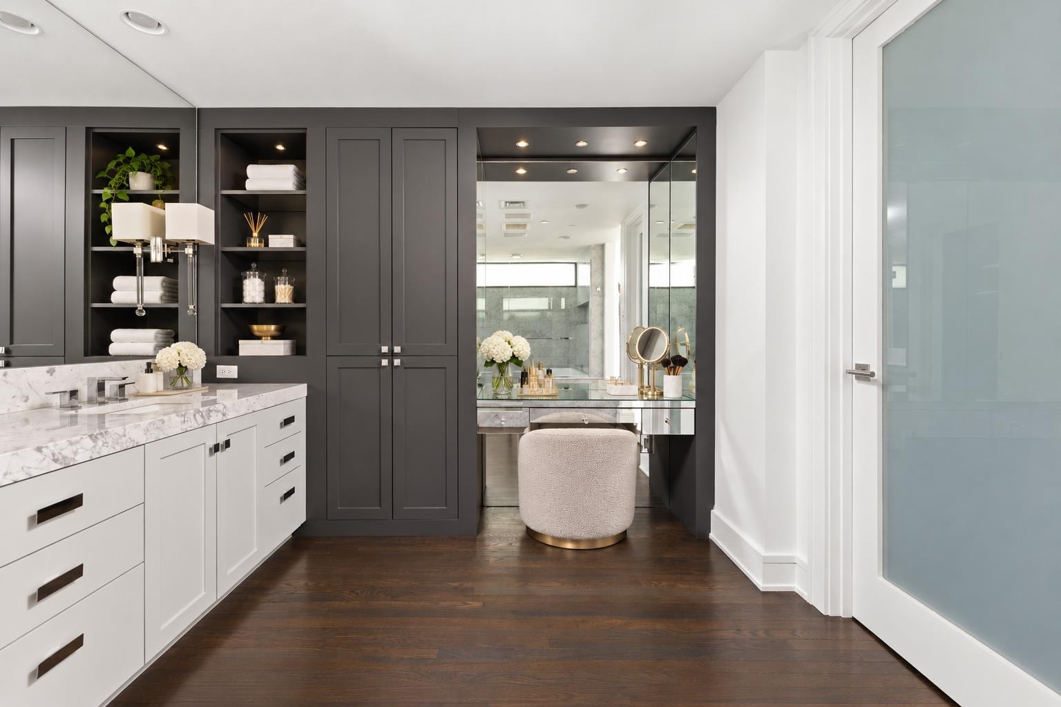 Bathroom with marble vanity, dark built-in cabinetry, and a mirrored makeup station.