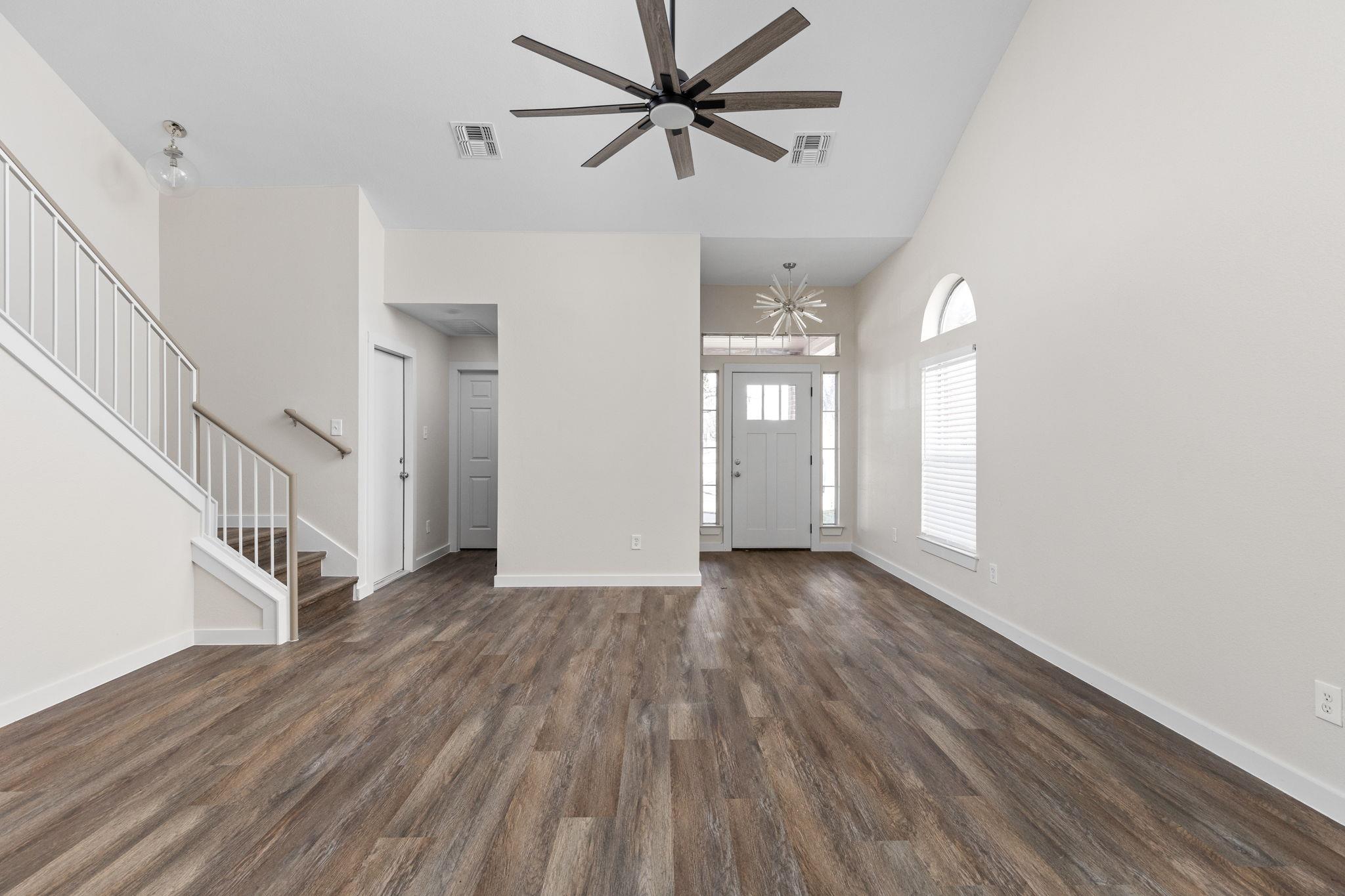 Vacant entryway with wood-look floors, a staircase, tall ceiling, and front door.