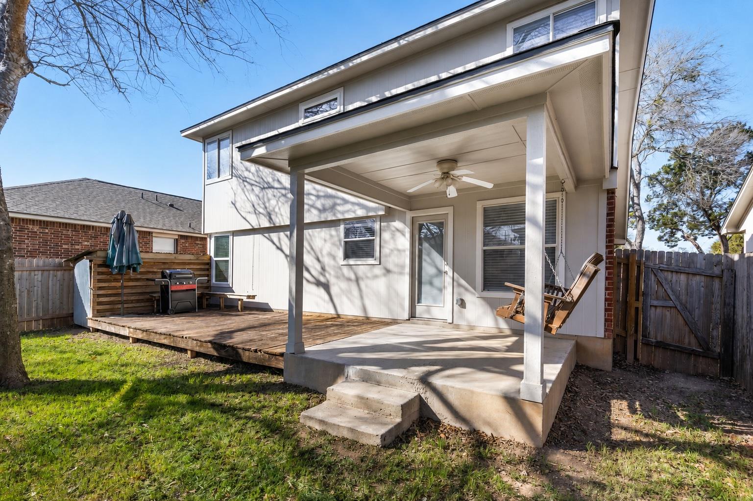 Rear of a two-story house with a covered patio, wooden deck, grill, and Adirondack chairs.