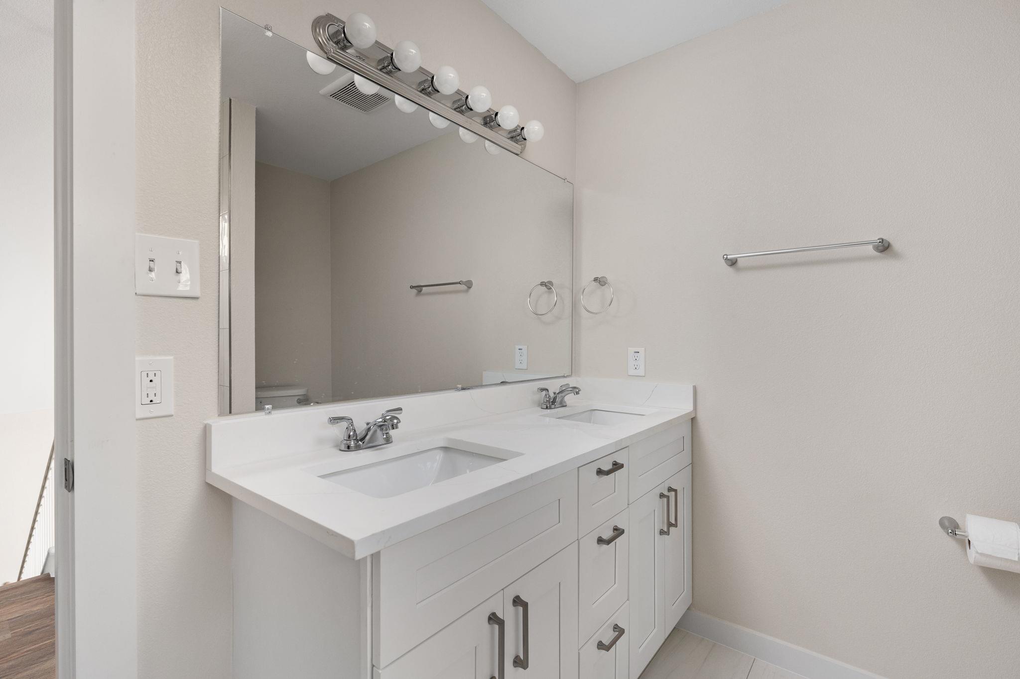 Bathroom with a white double-sink vanity, large mirror, and chrome fixtures.