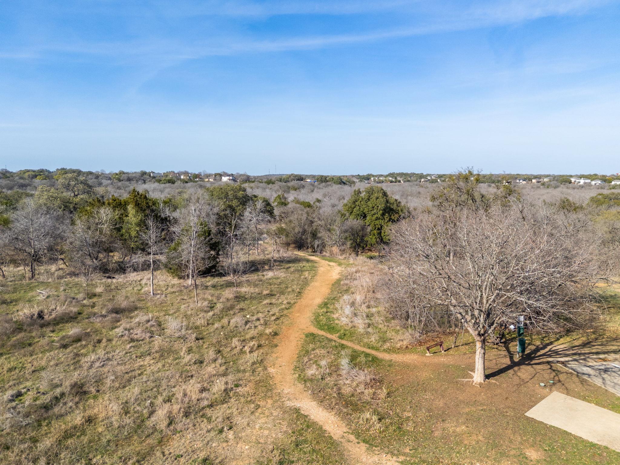 Wooded open space with a winding dirt trail, leafless trees, and distant homes.