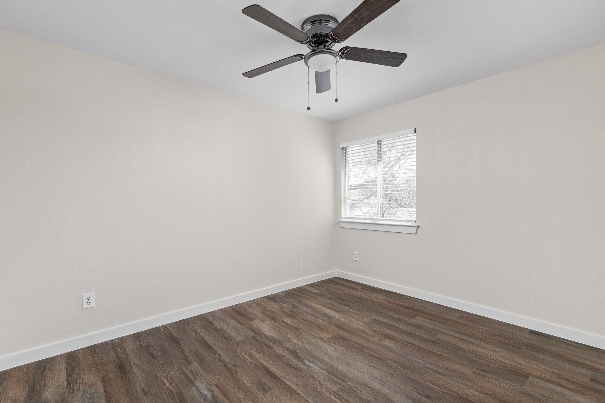 Empty bedroom with dark wood-look flooring, a ceiling fan, and a window with blinds.
