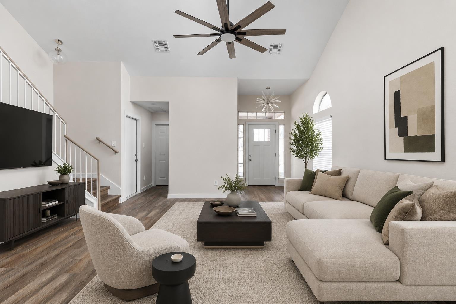 Staged living room with a cream sectional, high ceiling, staircase, and wood floors.
