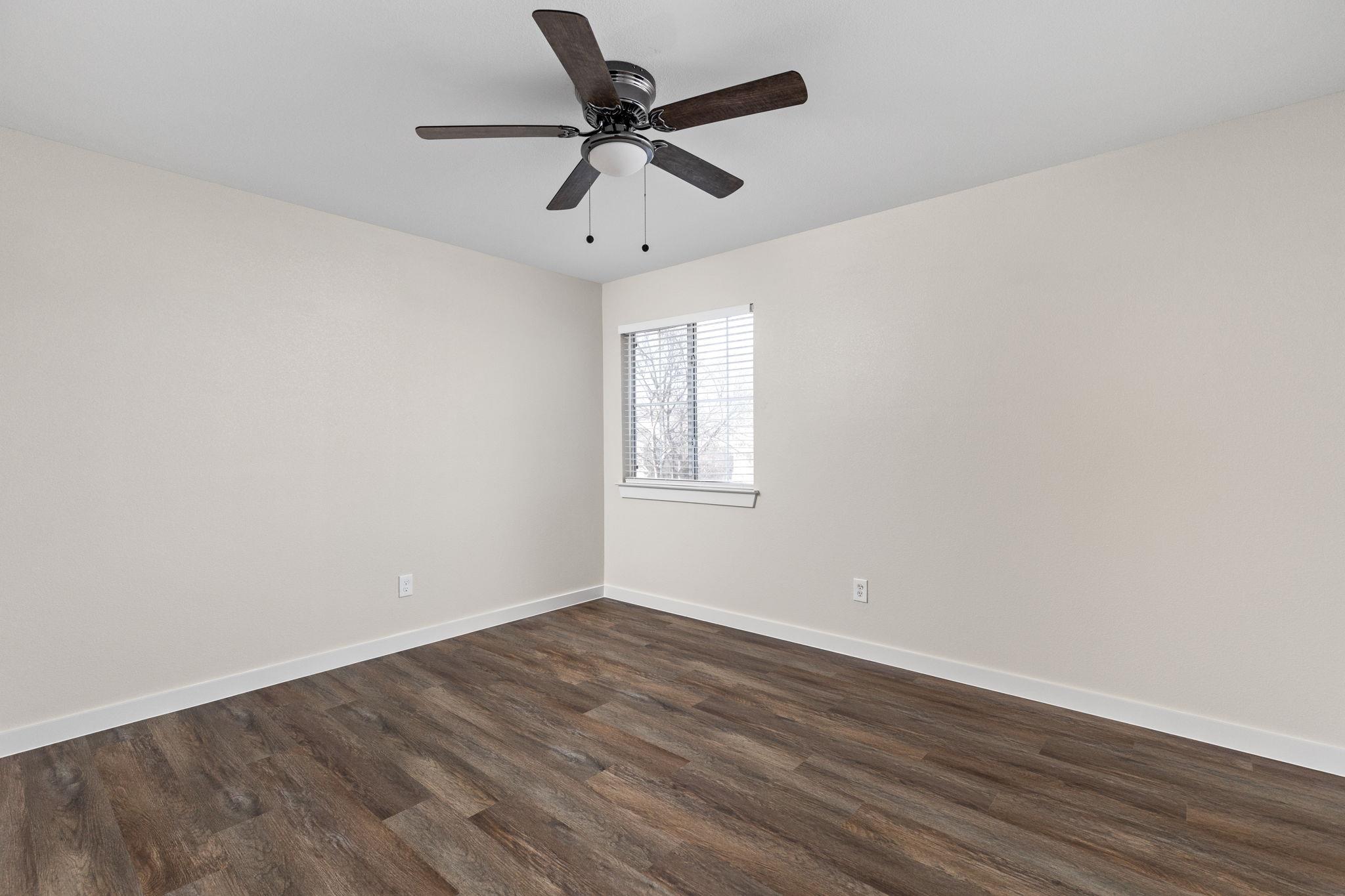 Vacant room with dark wood-look floors, a ceiling fan, and a window with blinds.