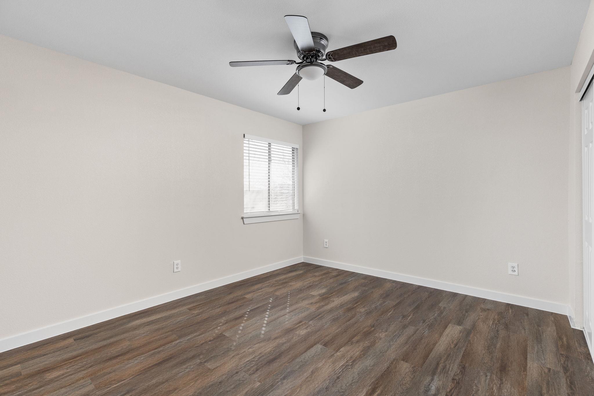 Empty room with dark wood-look flooring, a ceiling fan, and a window with white blinds.