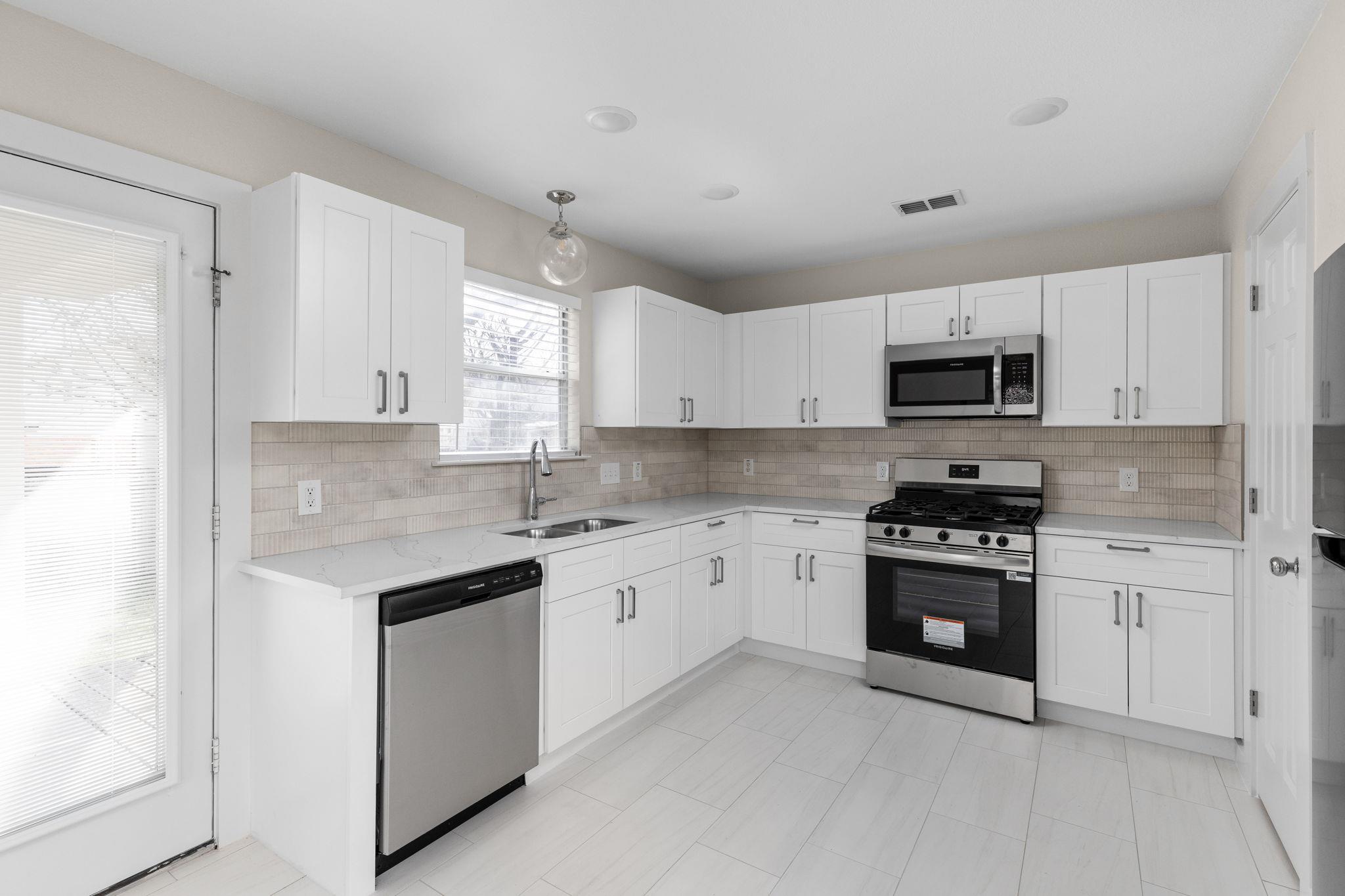 Kitchen with white shaker cabinets, stainless steel appliances, pale tile backsplash, and a sink beneath a window.