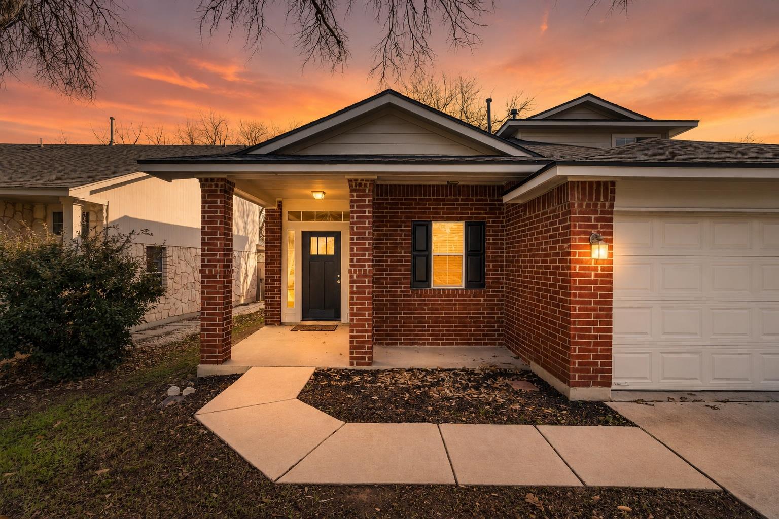 Red brick house with a covered entry, attached garage, and curved walkway at dusk.