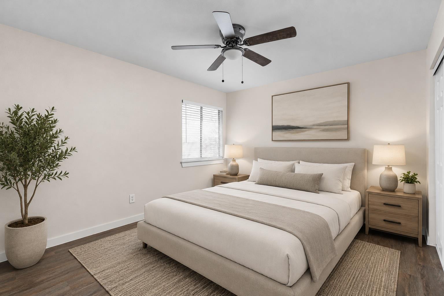 Staged bedroom with a large upholstered bed, matching wood nightstands, and a ceiling fan.