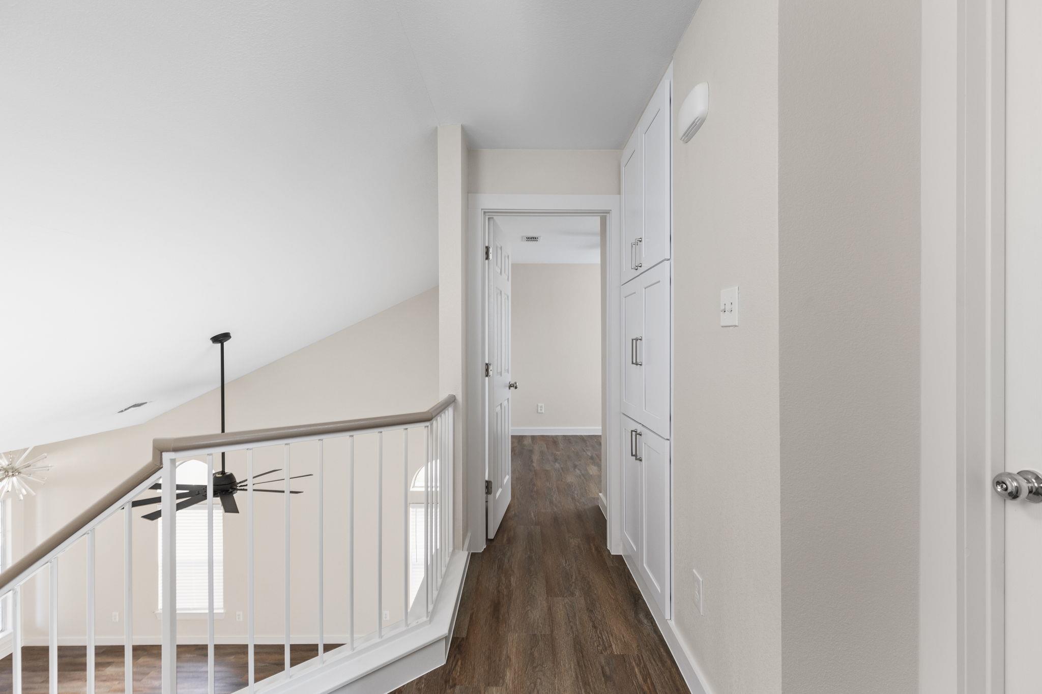 Upstairs hallway with dark wood flooring, white built-in cabinets, and a railing overlooking the stairwell.
