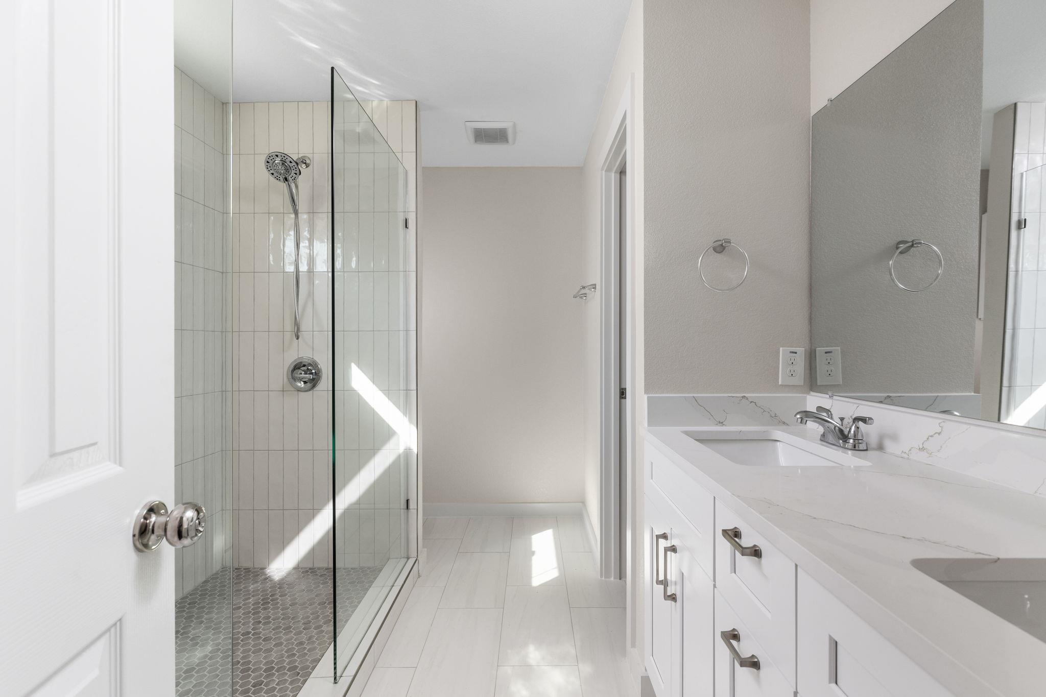 Bright bathroom with a glass walk-in shower and white double vanity with marble-look counters.