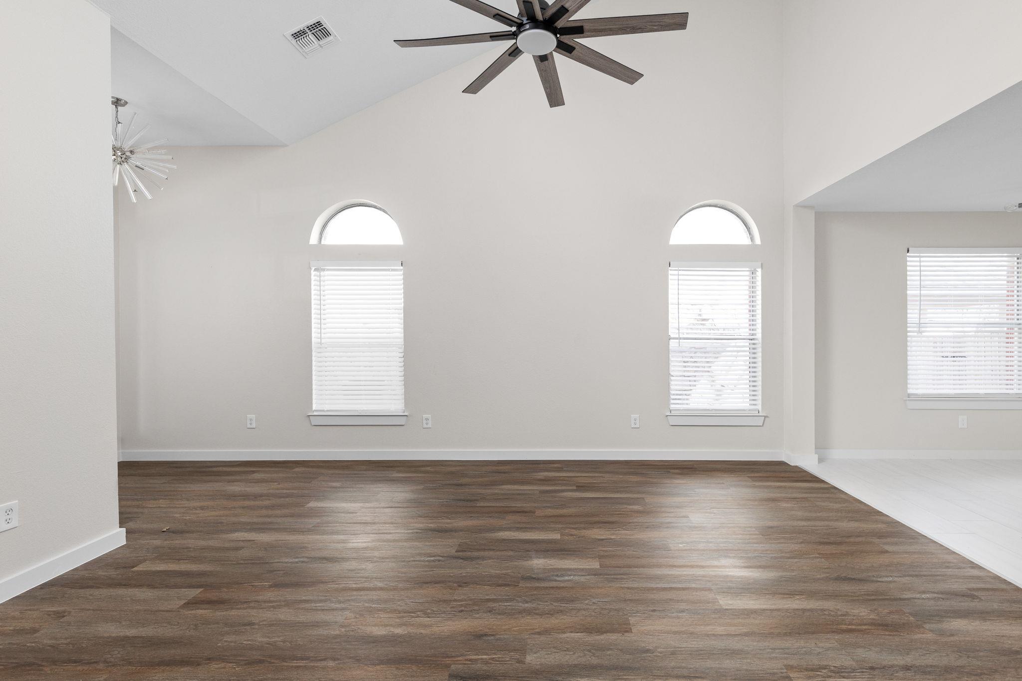 Vacant living room with dark wood-look floors, a high ceiling, and arched windows.