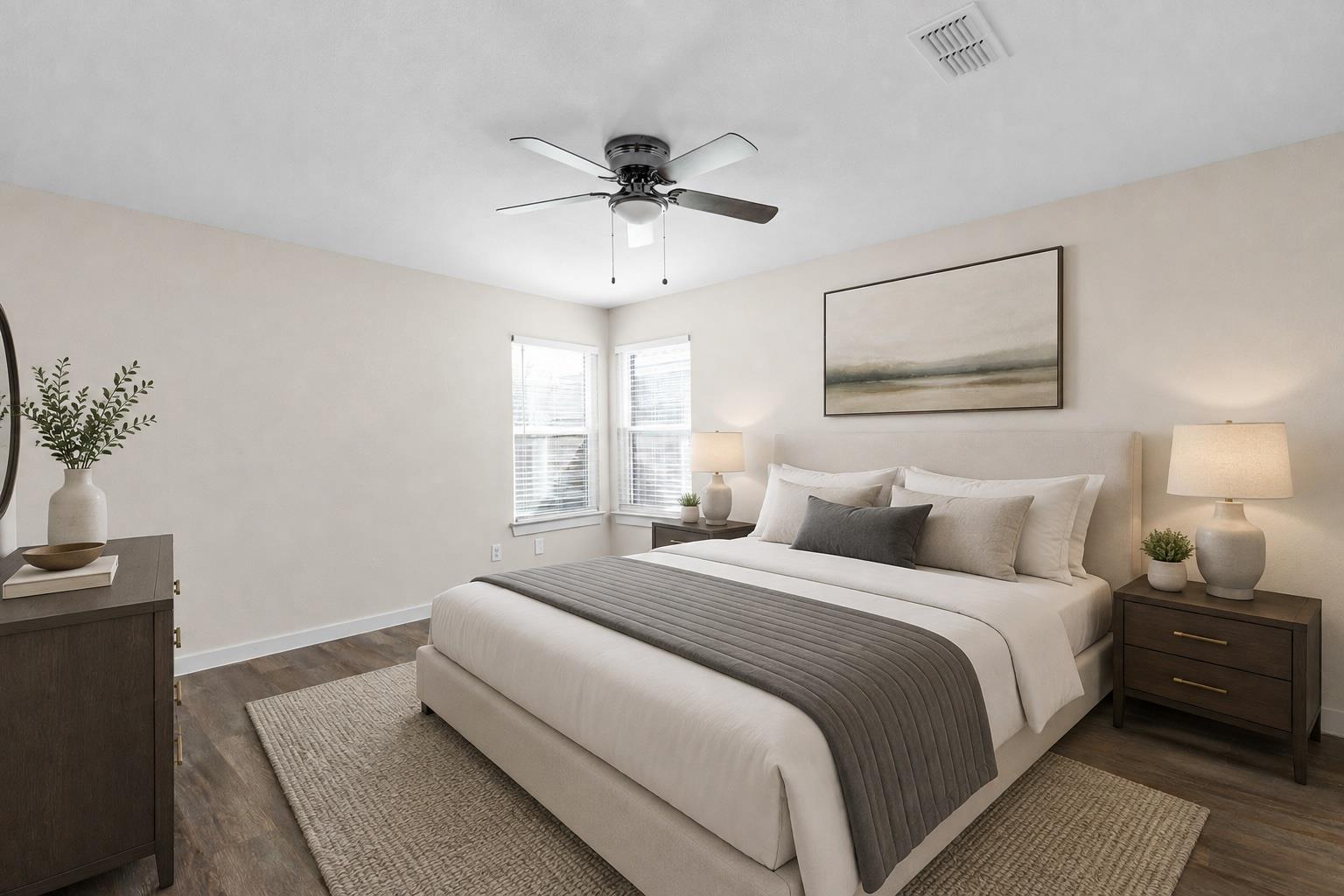 Staged bedroom with an upholstered bed, gray runner, dark wood nightstands, and ceiling fan.