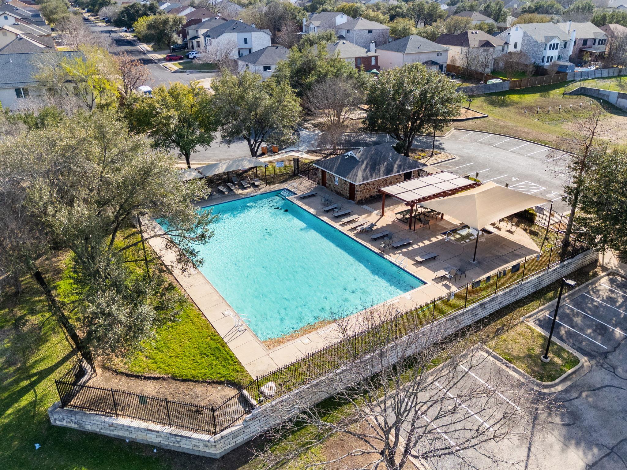 Neighborhood swimming pool with shaded lounge areas and a stone pool house, seen from above.