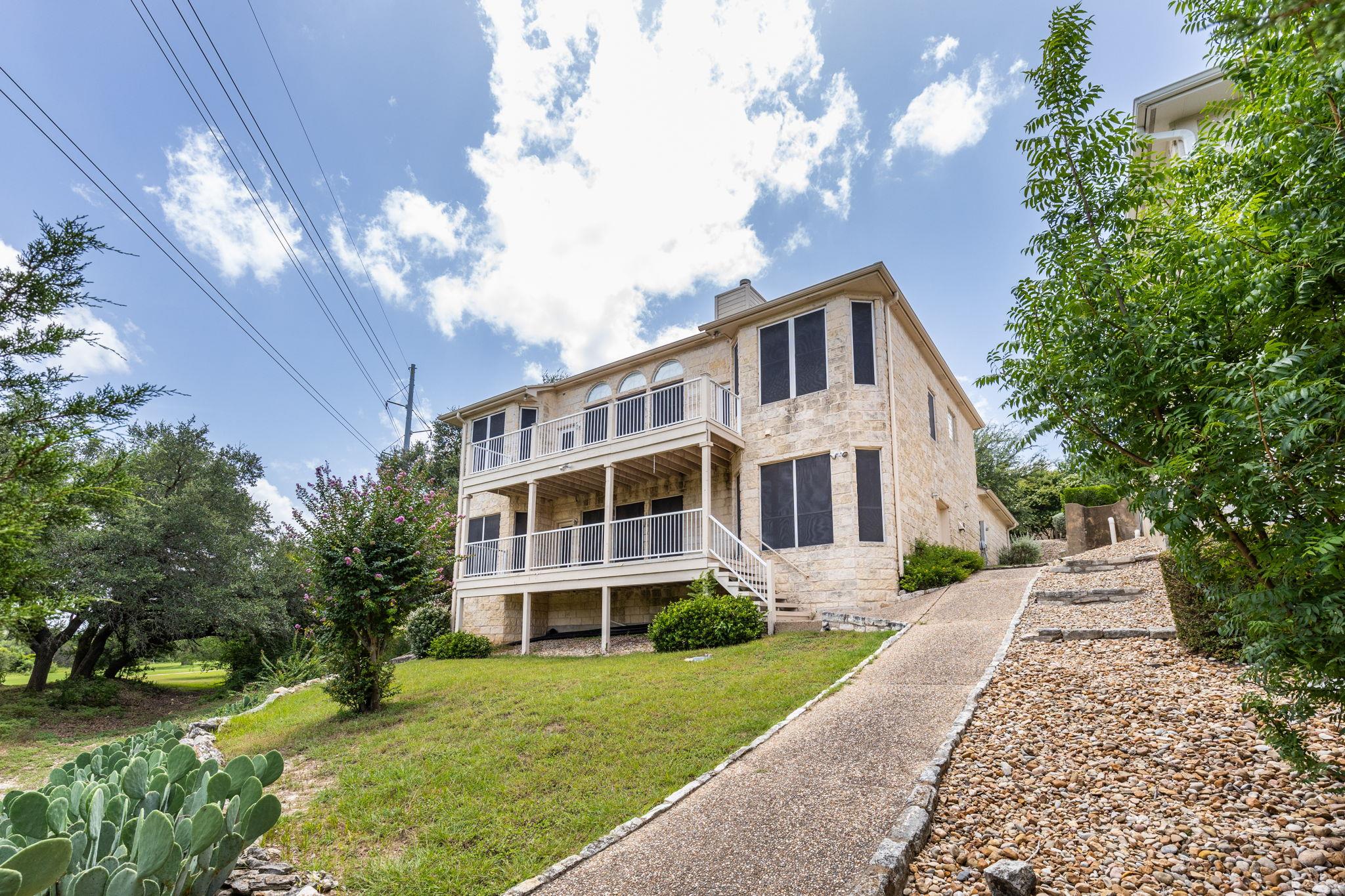 Light stone house with two covered balconies above a sloping landscaped yard.