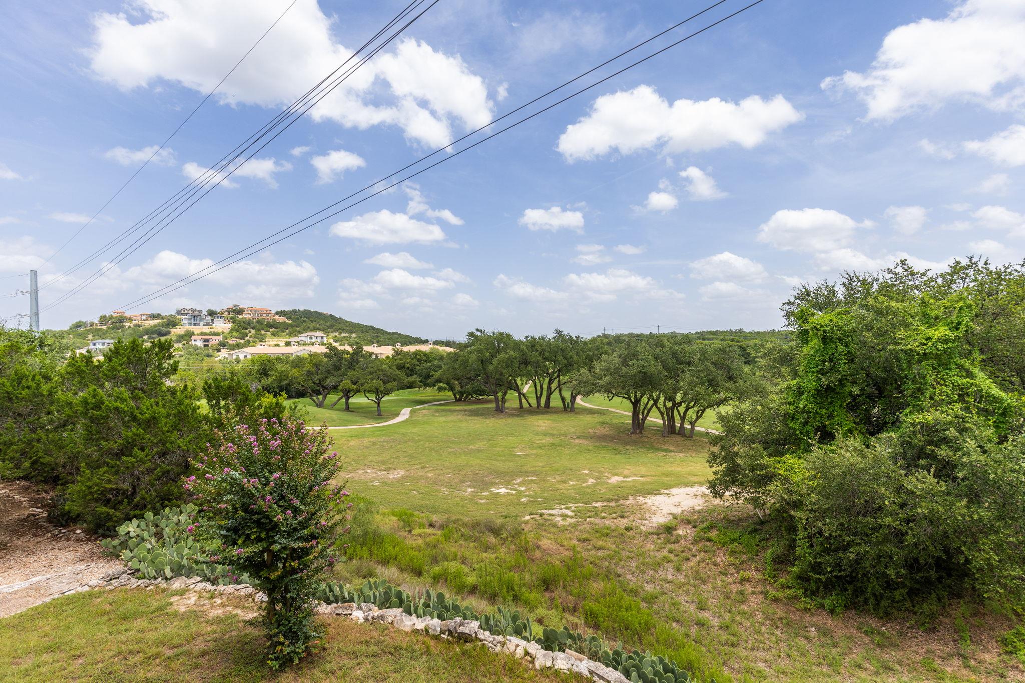 Golf course with a winding path, mature trees, and hillside homes beyond prickly pear cactus.