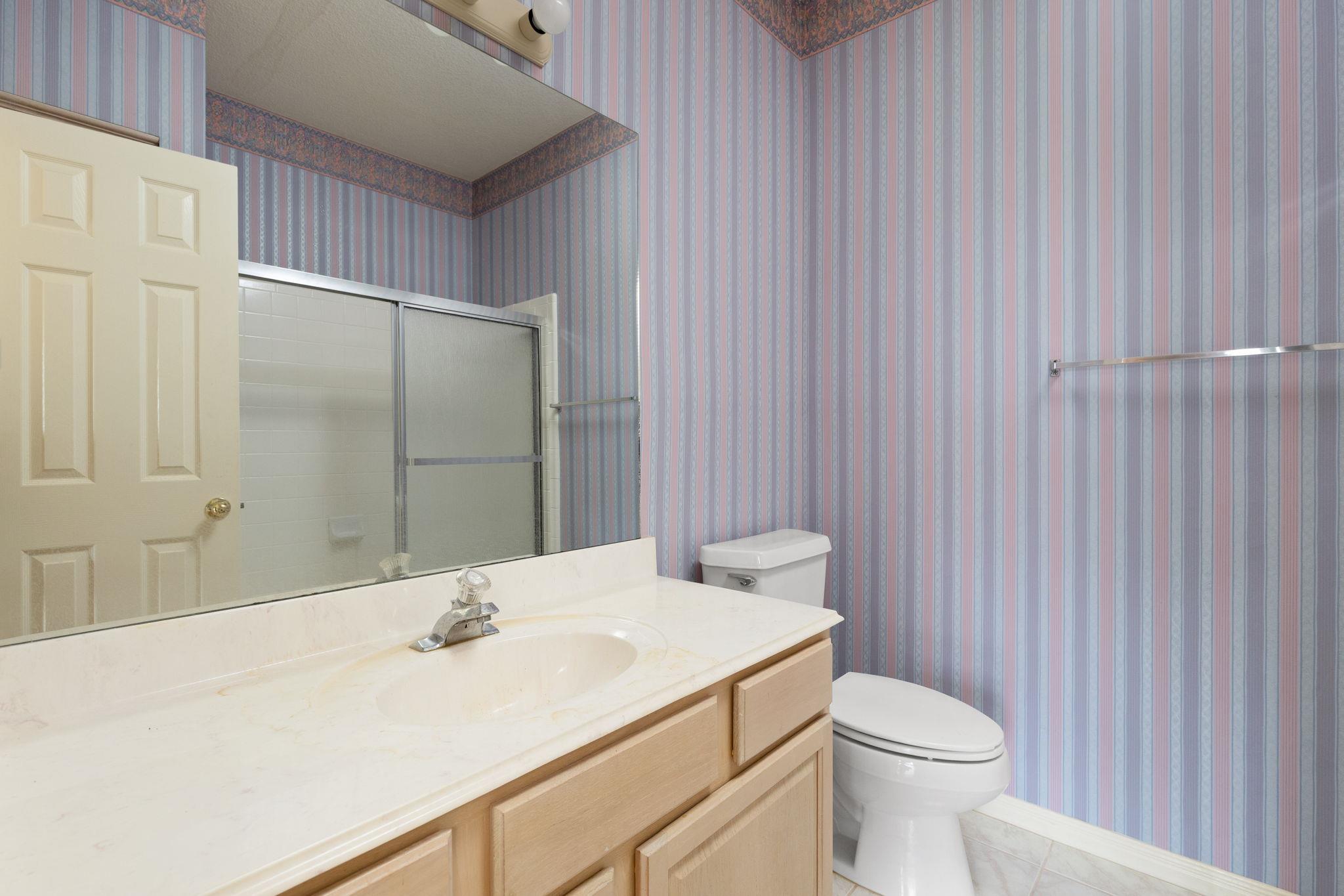 Bathroom with a light wood vanity, glass shower enclosure, and blue-and-pink striped wallpaper.