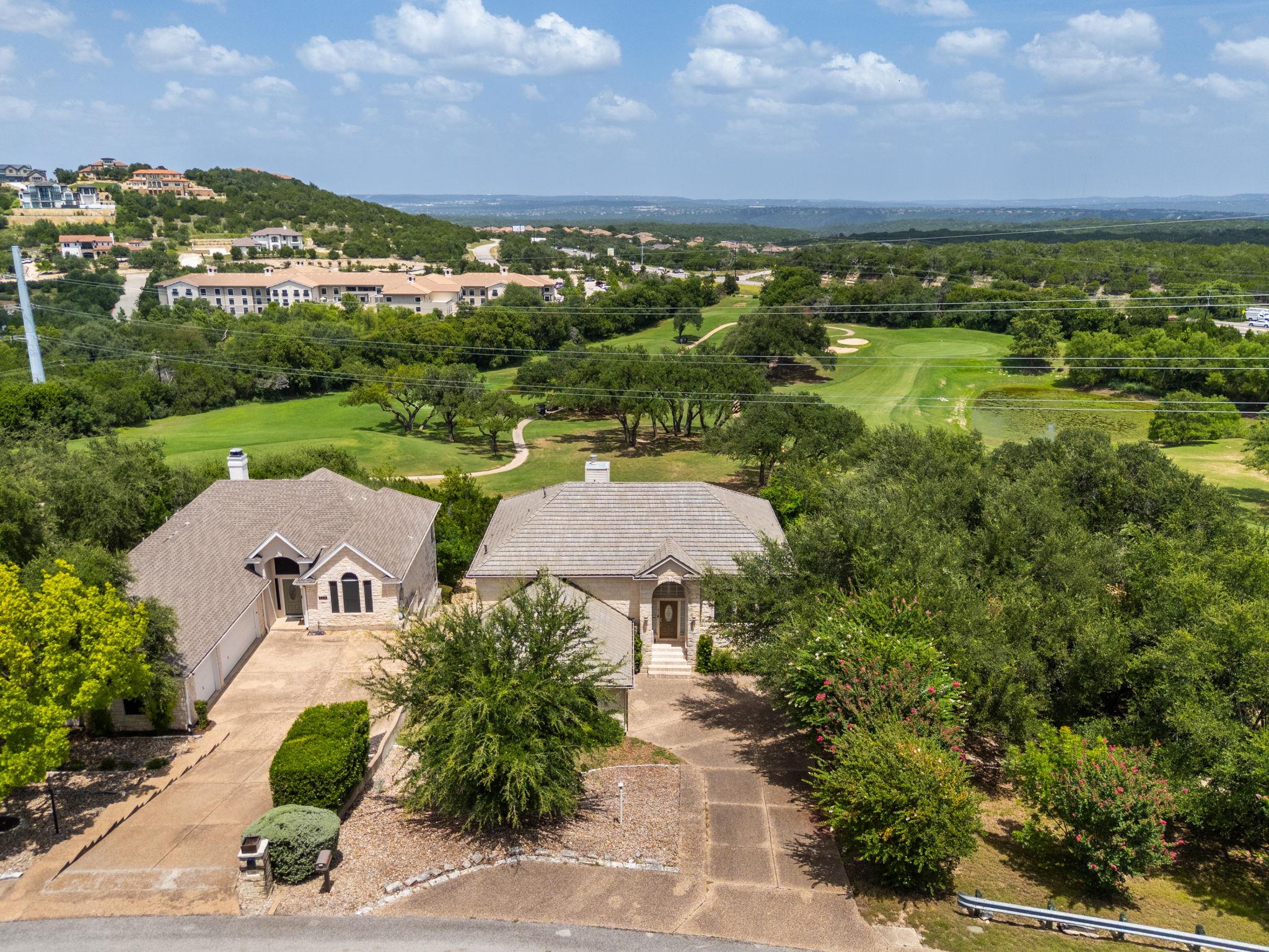 Aerial view of a stone home overlooking a green golf course with wooded hills beyond.