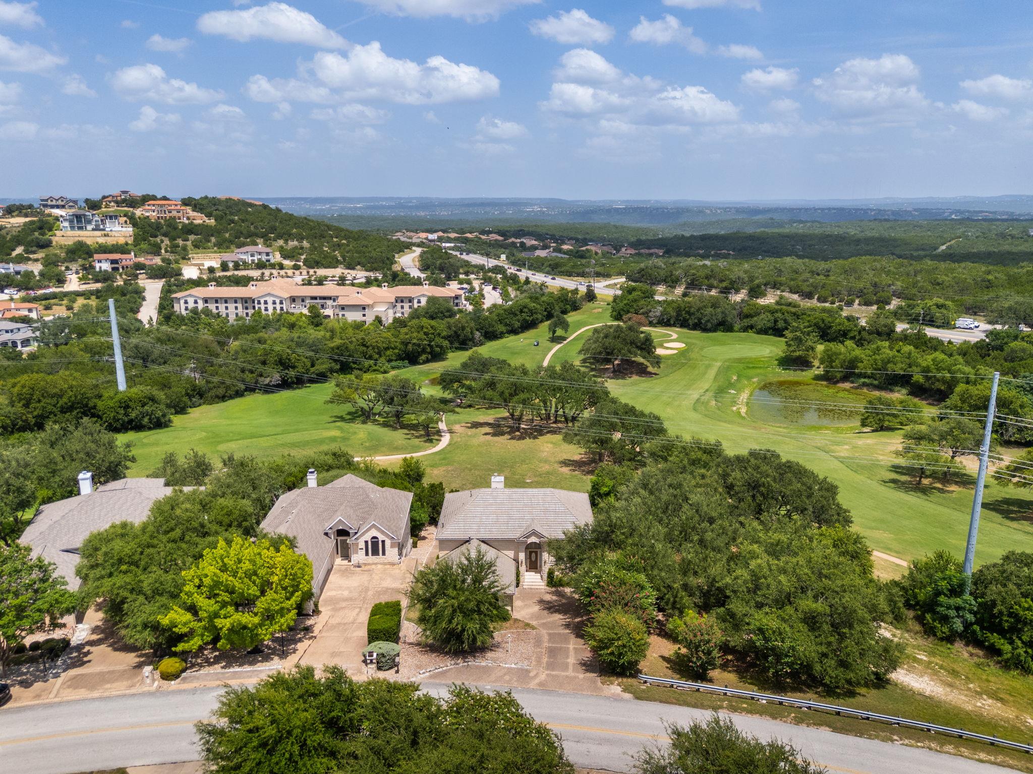 Aerial view of homes beside a golf course, with fairways, trees, and distant hills.