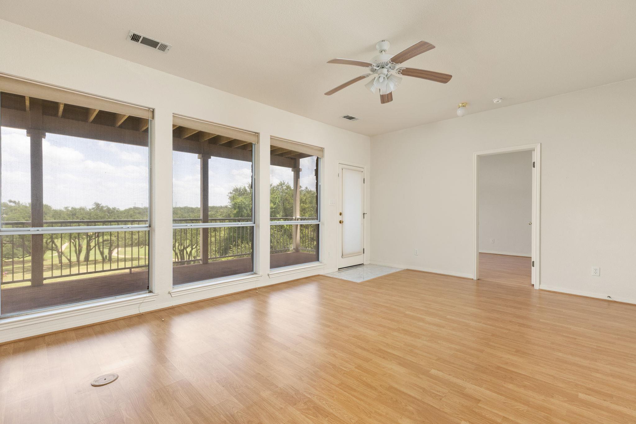 Vacant living room with wood flooring, a ceiling fan, and large windows overlooking the golf course.