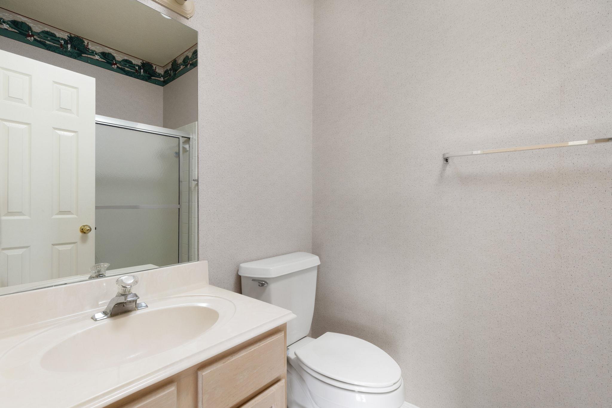 Bathroom with a light wood vanity, white sink, toilet, and frosted-glass shower.
