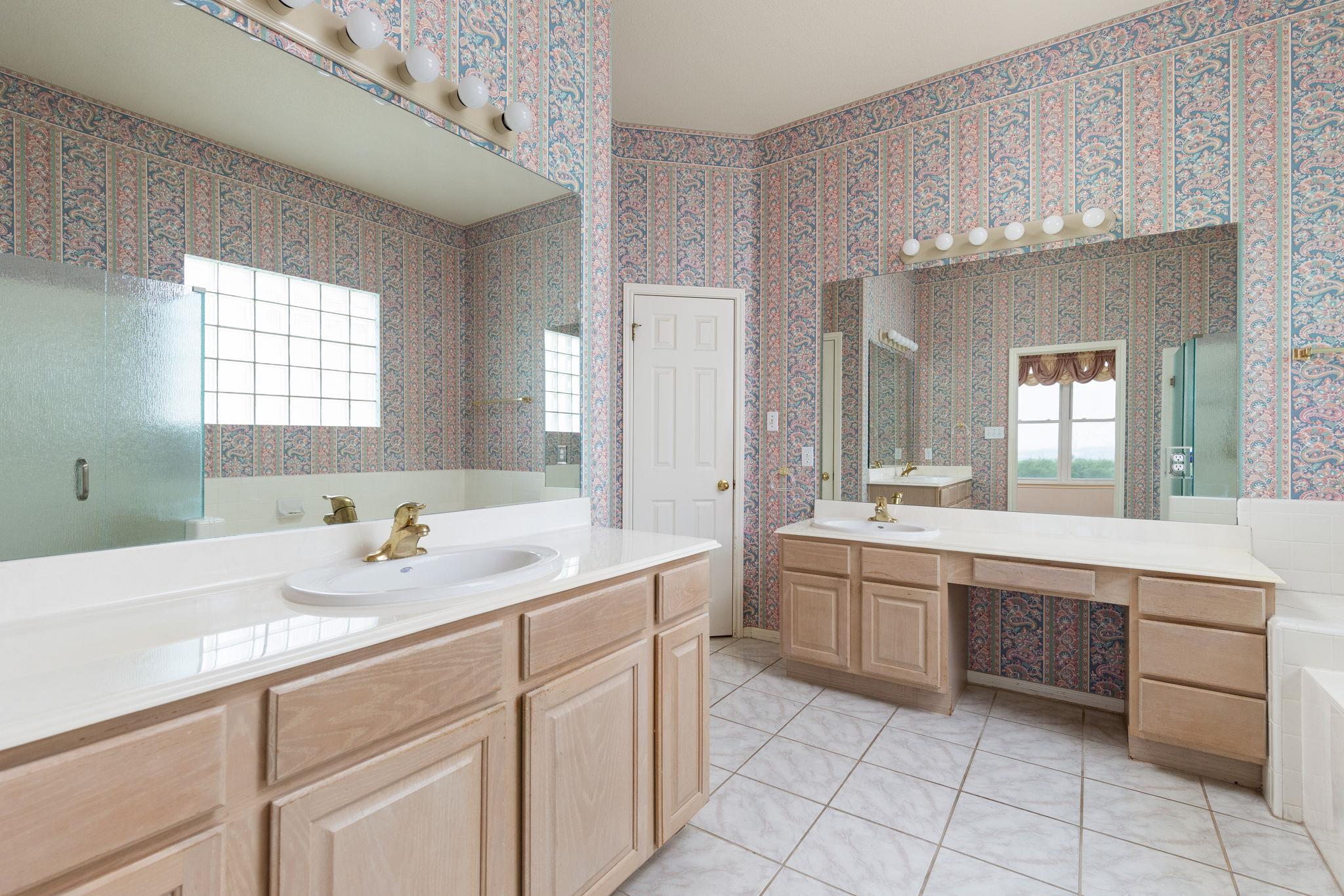 Bathroom with patterned wallpaper, mirrored walls, and a long double-sink vanity.