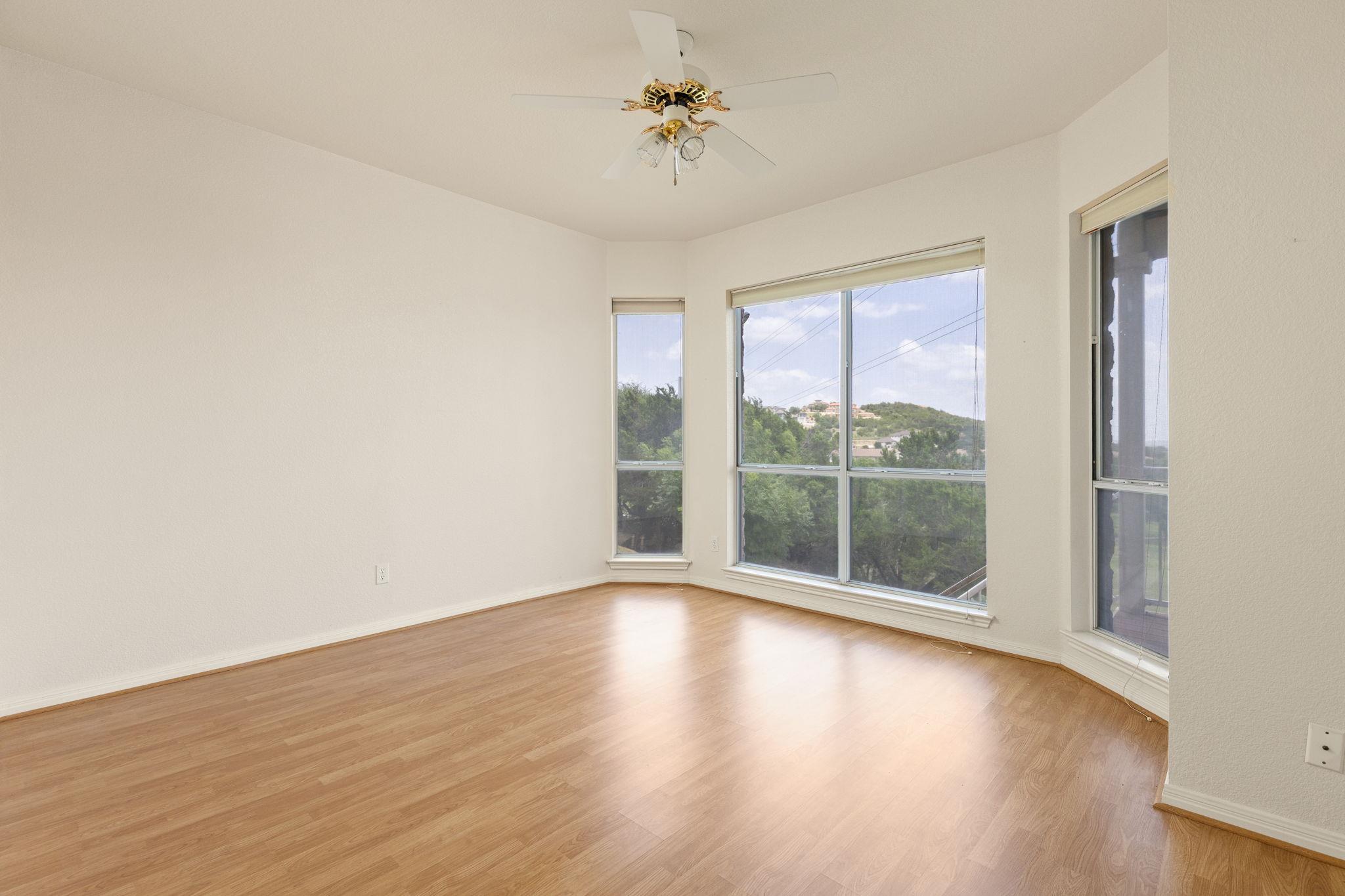 Empty room with wood floors, a ceiling fan, and large windows overlooking green hills.