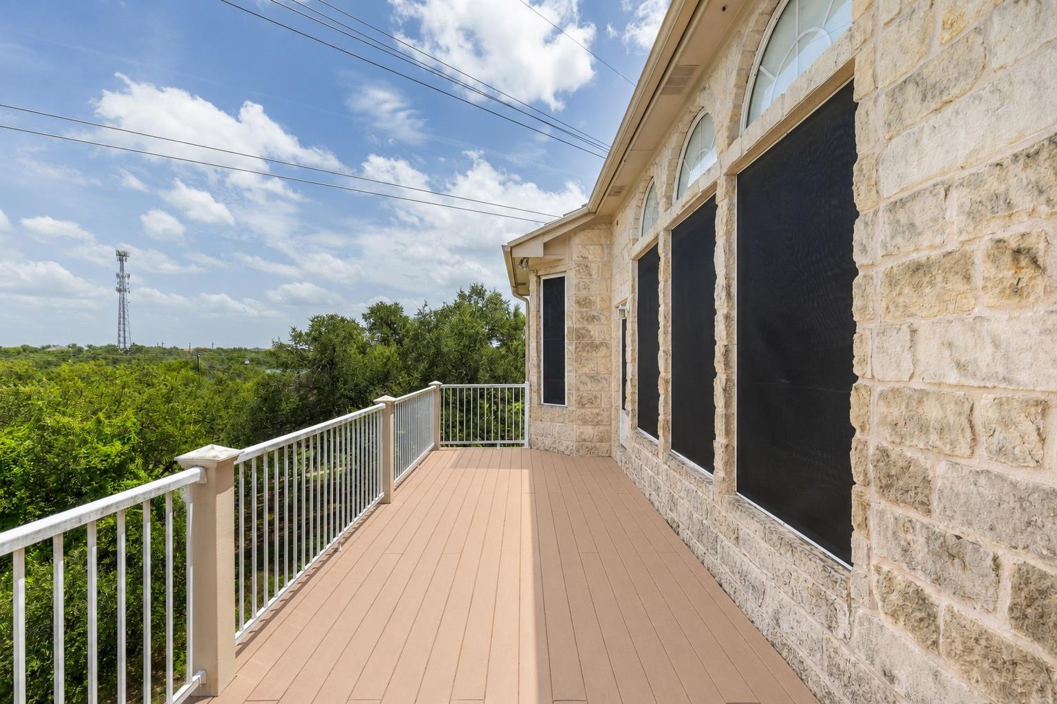 Elevated deck beside a limestone exterior, with white railing and leafy views.
