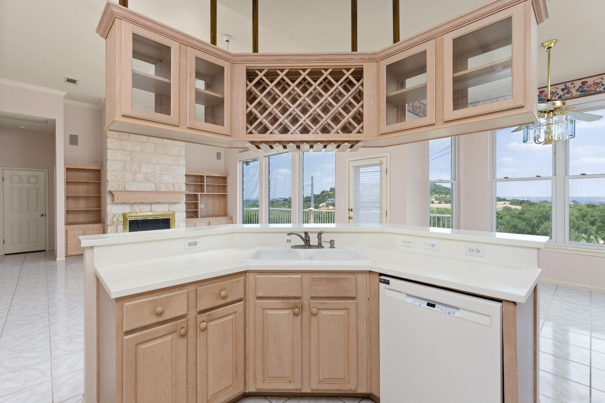 Kitchen with a curved wood island, diamond-lattice wine rack, stone fireplace, and large windows.