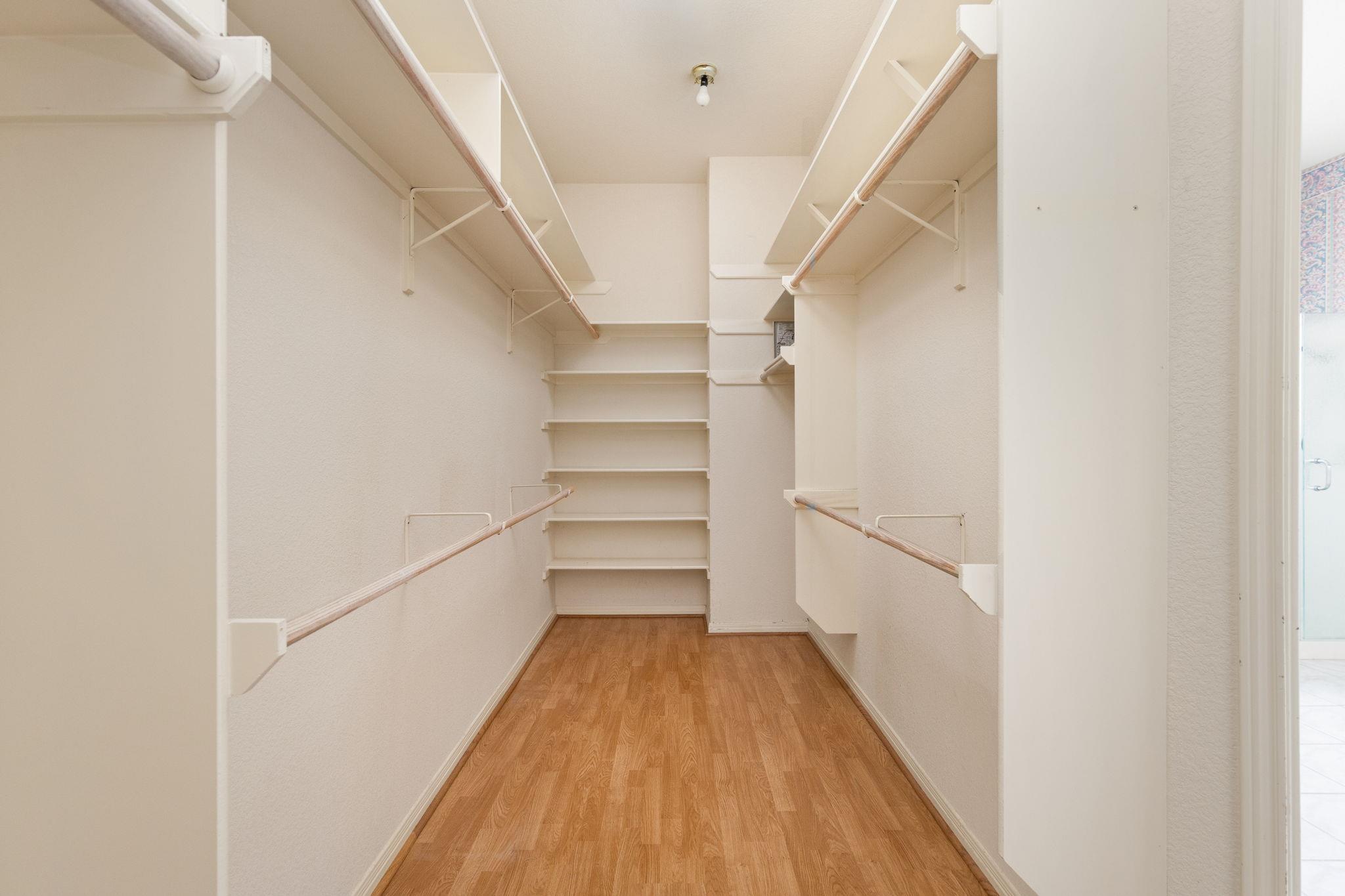 Empty walk-in closet with built-in shelving, hanging rods, and wood flooring.