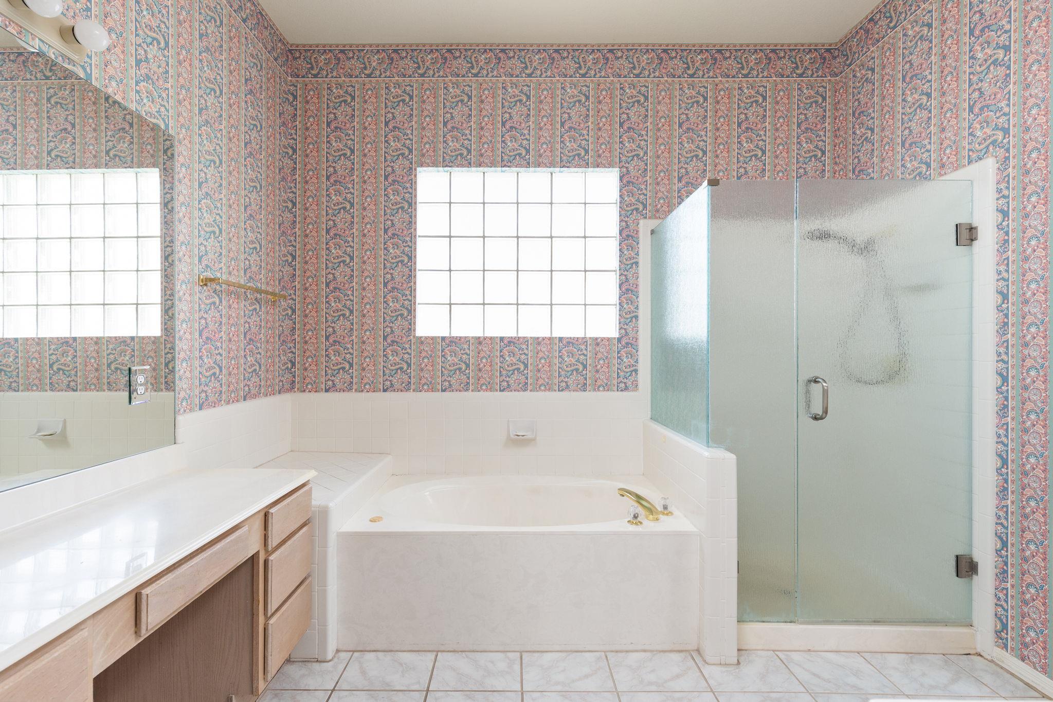 Bathroom with a soaking tub, frosted-glass shower, and colorful patterned wallpaper.