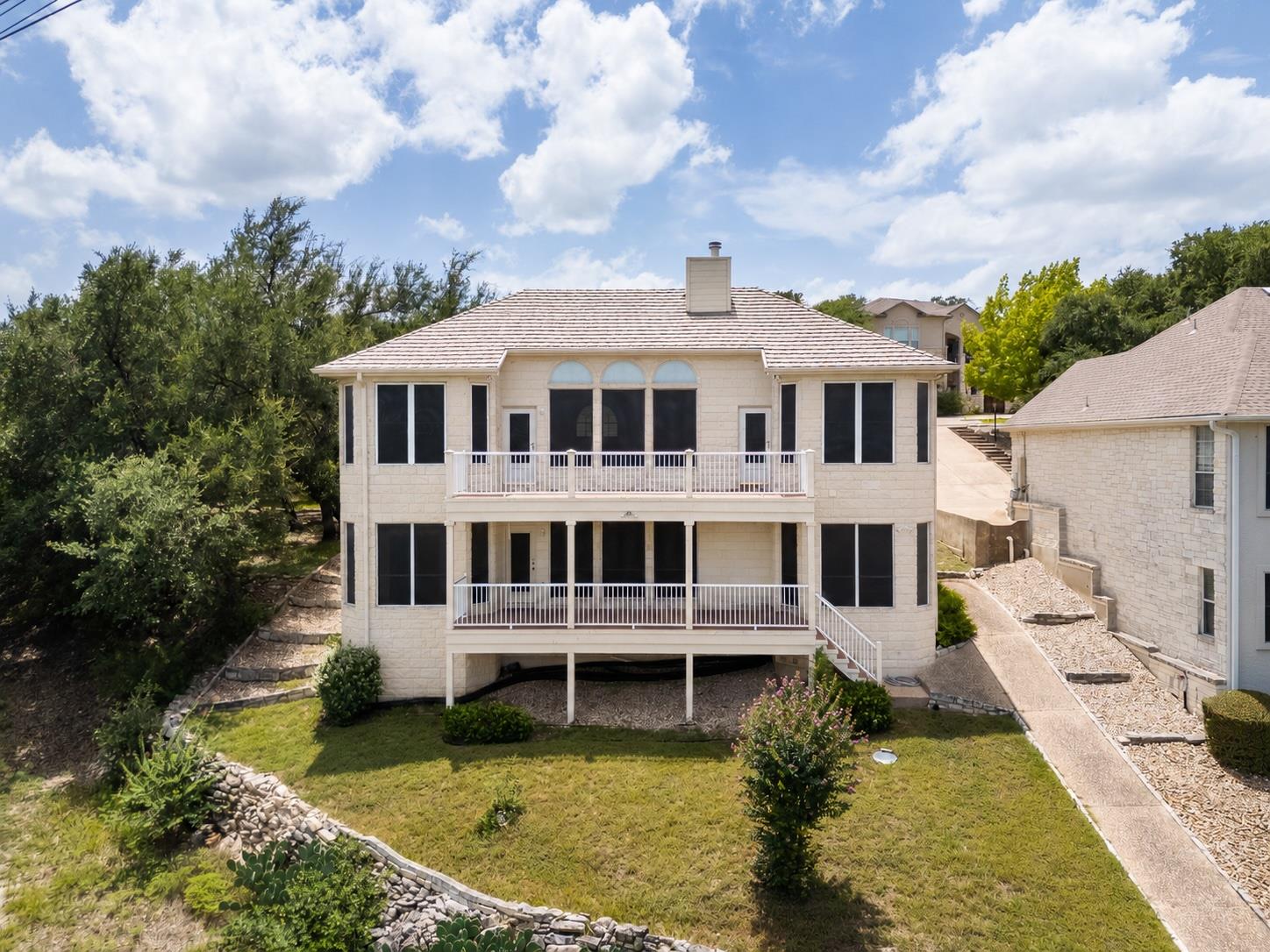 Rear of a two-story stone home with two balconies and a landscaped sloping yard.