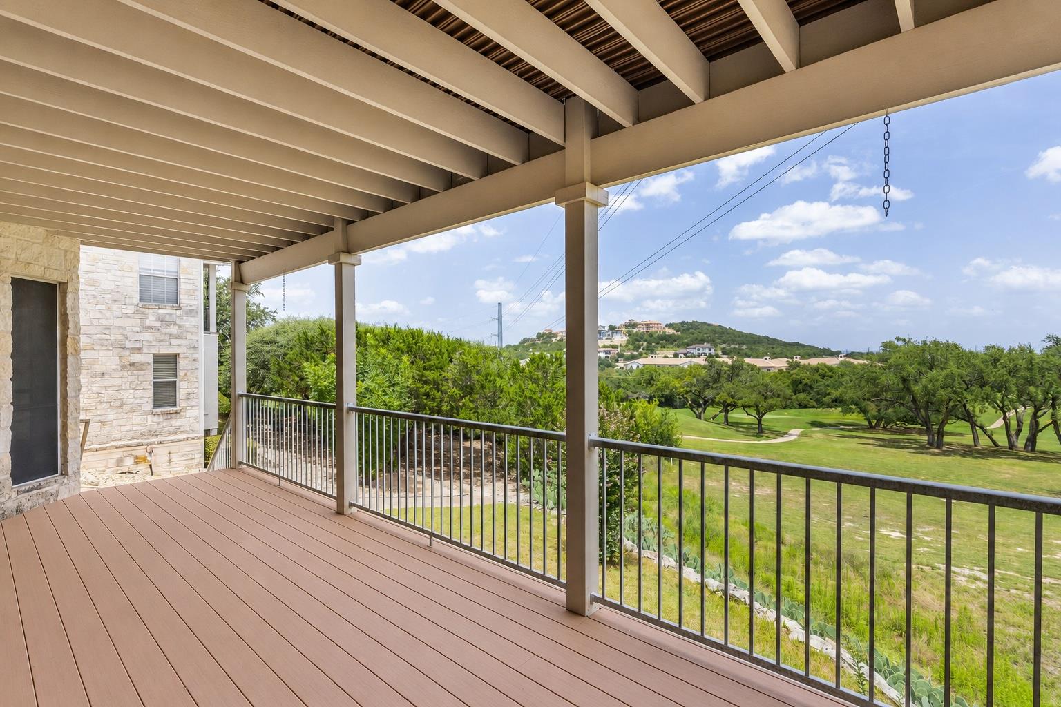 Covered deck overlooking a golf course, with metal railings and a stone-clad home.