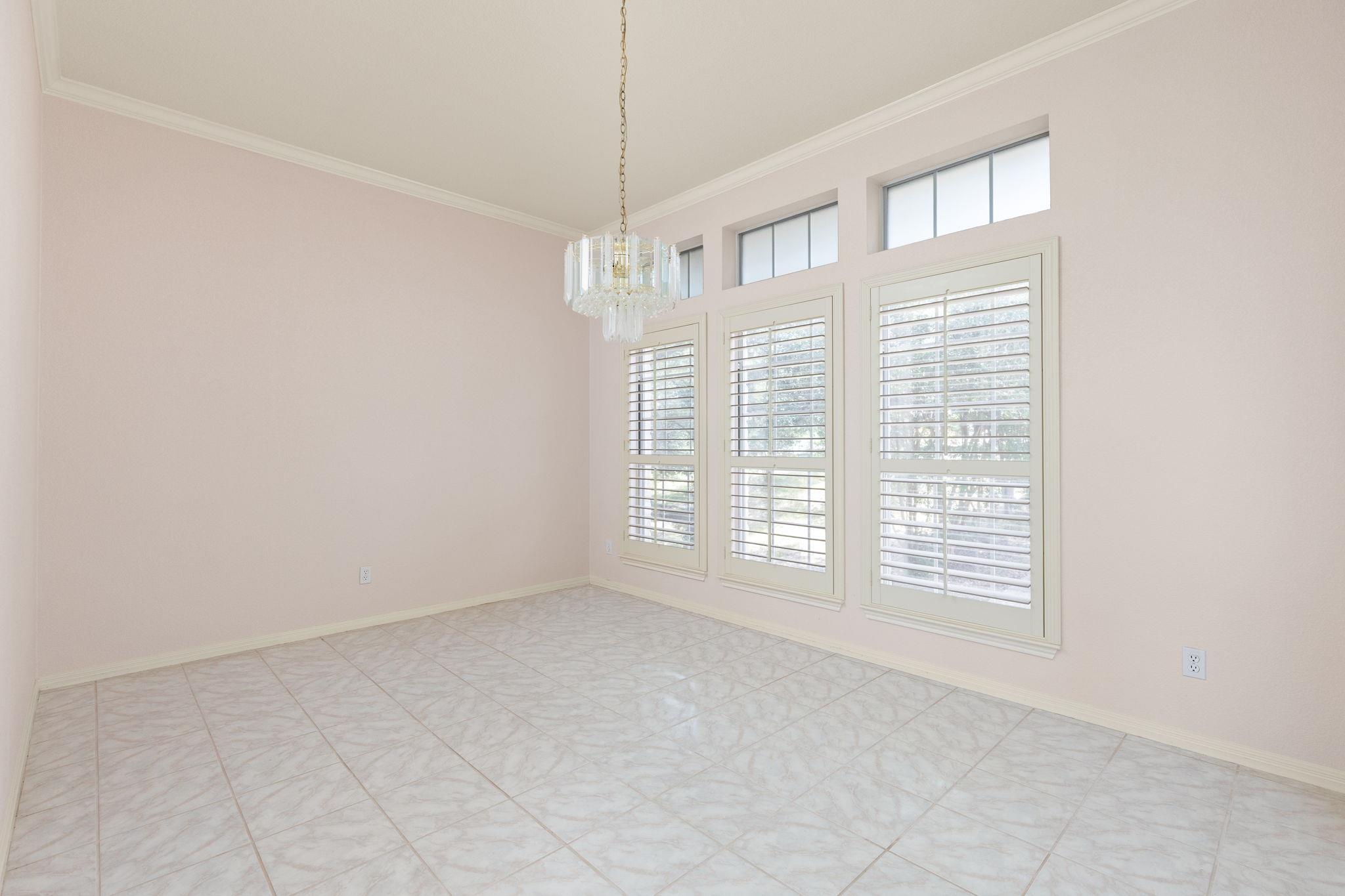 Empty dining room with tiled floors, plantation shutters, and a chandelier.