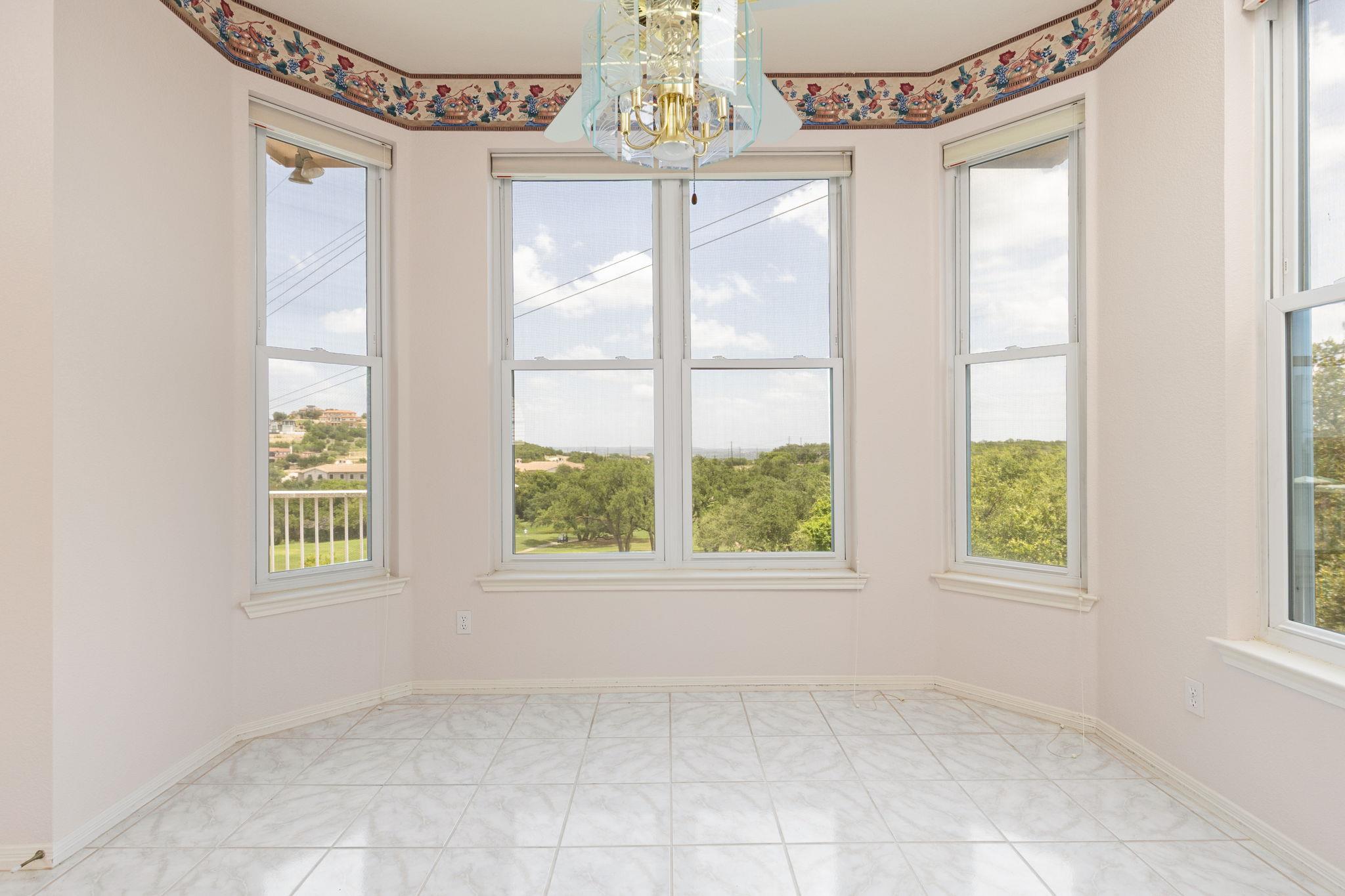 Empty tiled room with tall curved windows, a glass chandelier, and views of green trees.