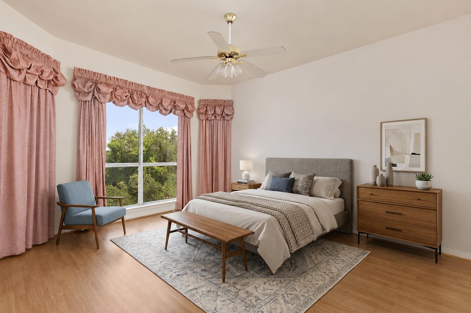 Staged bedroom with a gray bed, blue armchair, and large windows framed by pink curtains.