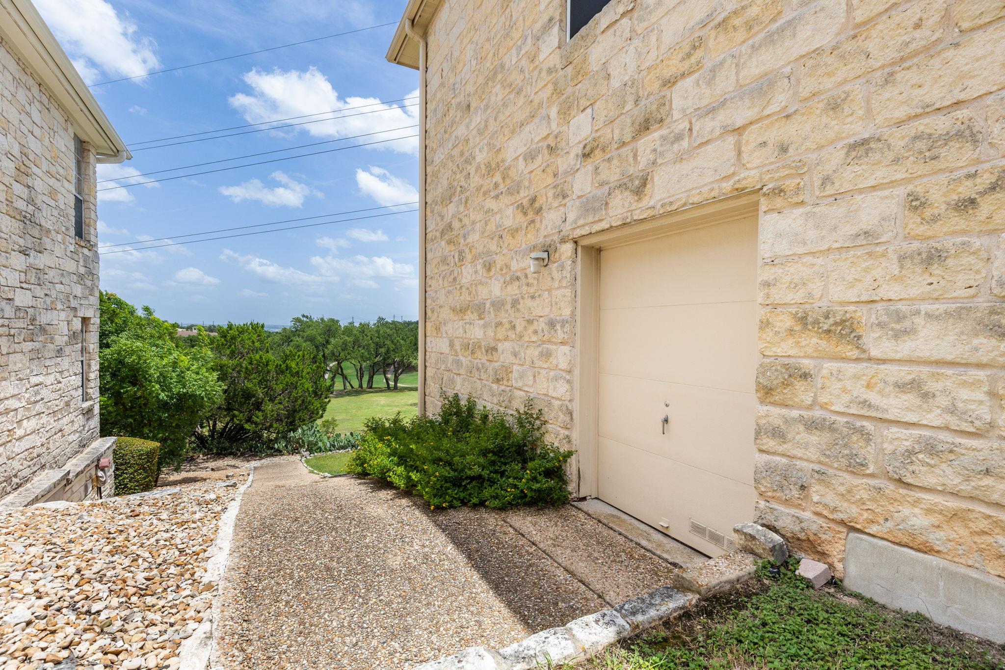 Stone house exterior with garage door, landscaped walkway, and green lawn beyond.