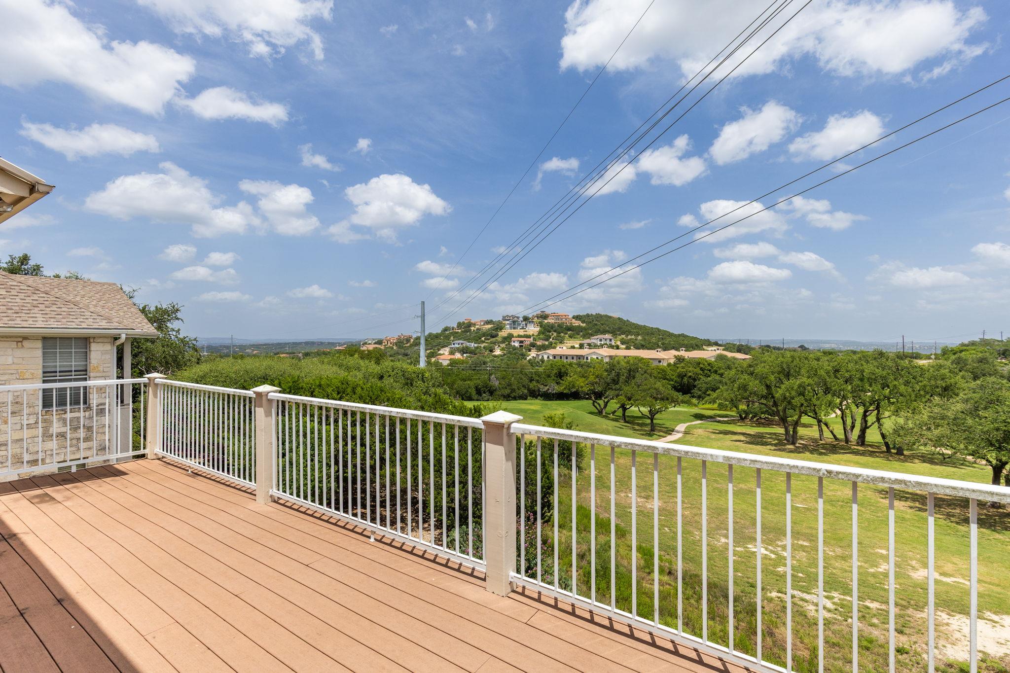 Wood deck overlooking a tree-lined golf course and homes on a distant hill.