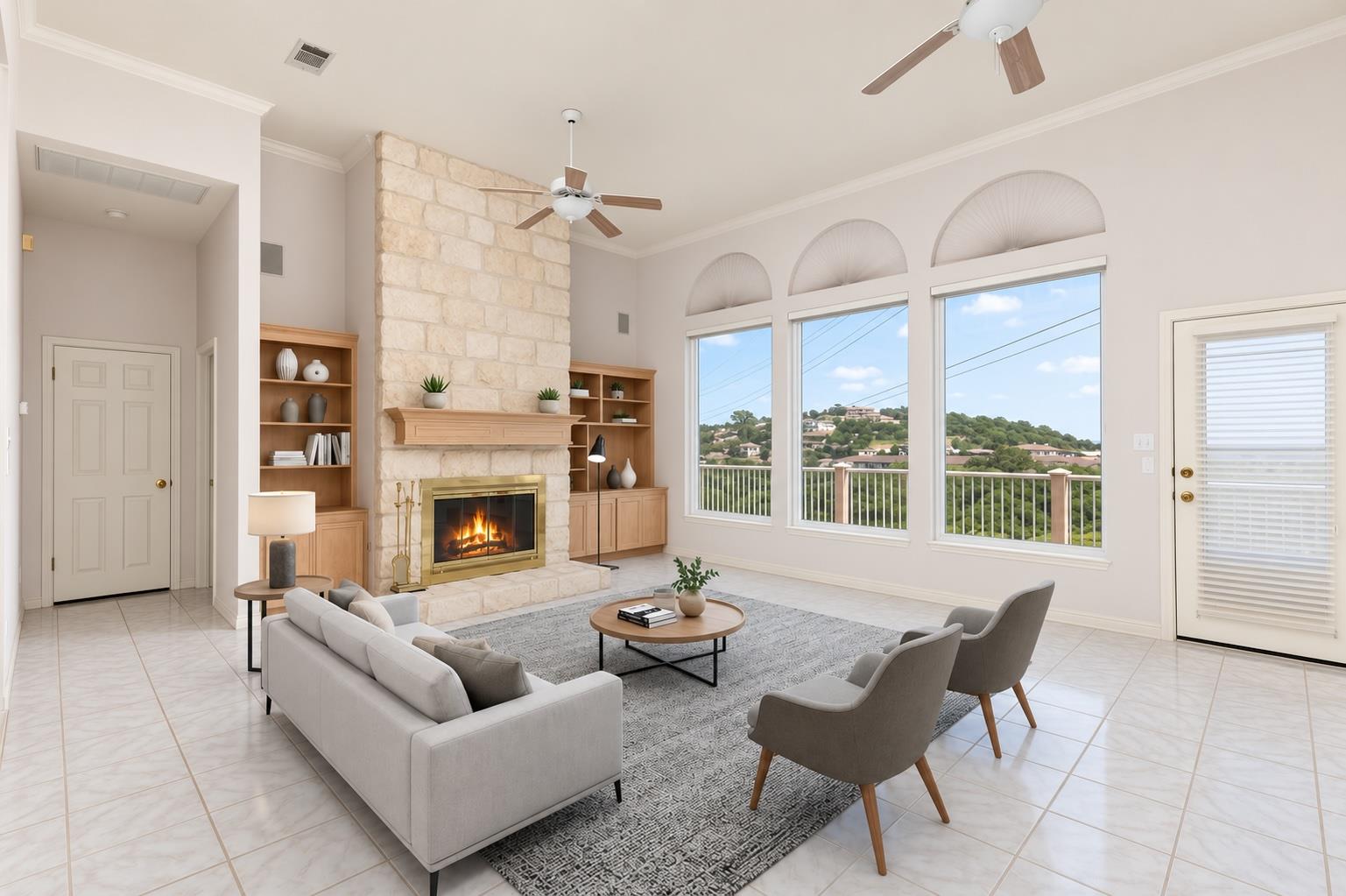 Living room with a stone fireplace, arched windows, and views of a green hillside neighborhood.