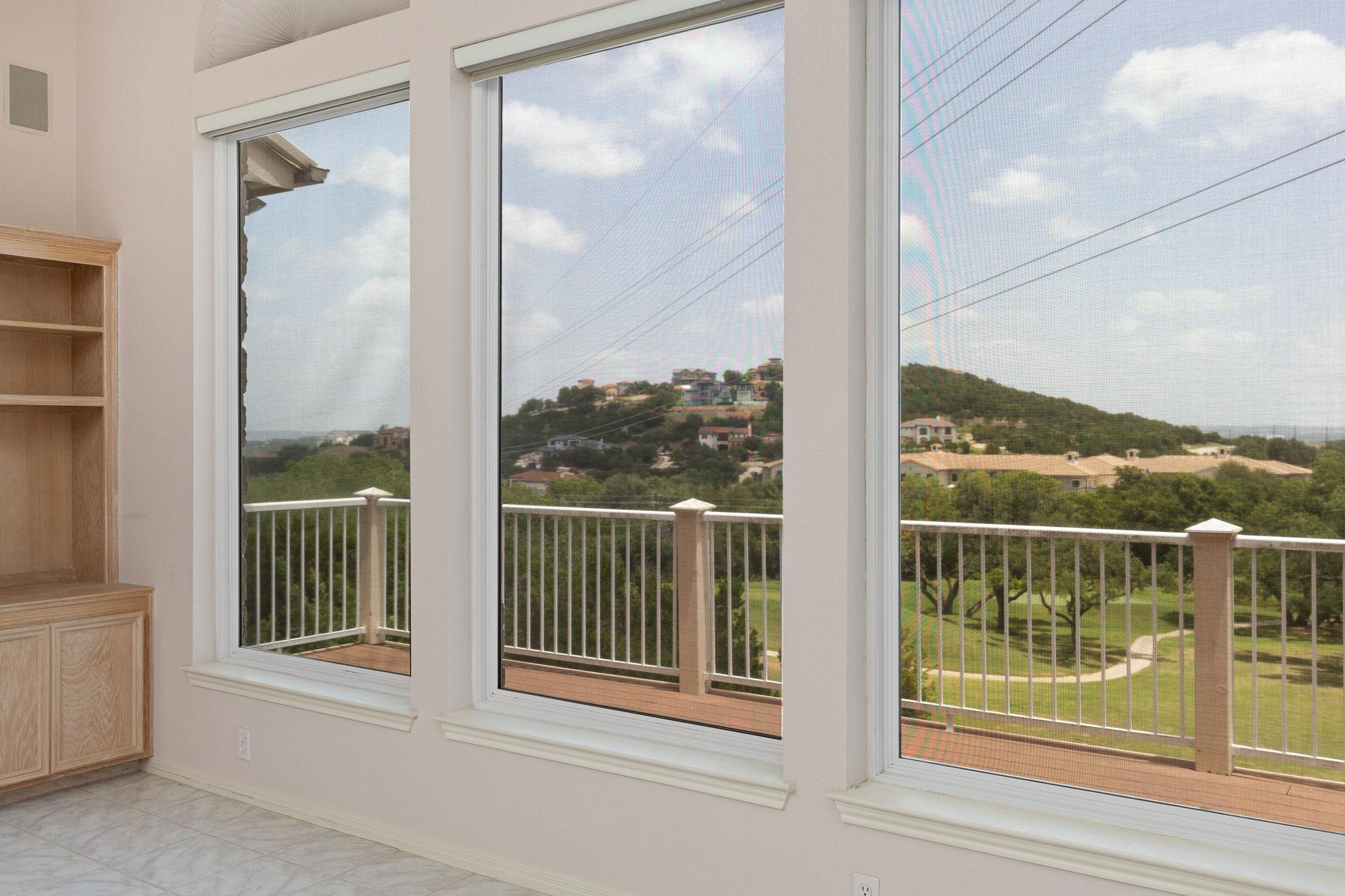 Empty room with large windows overlooking a balcony and golf course.